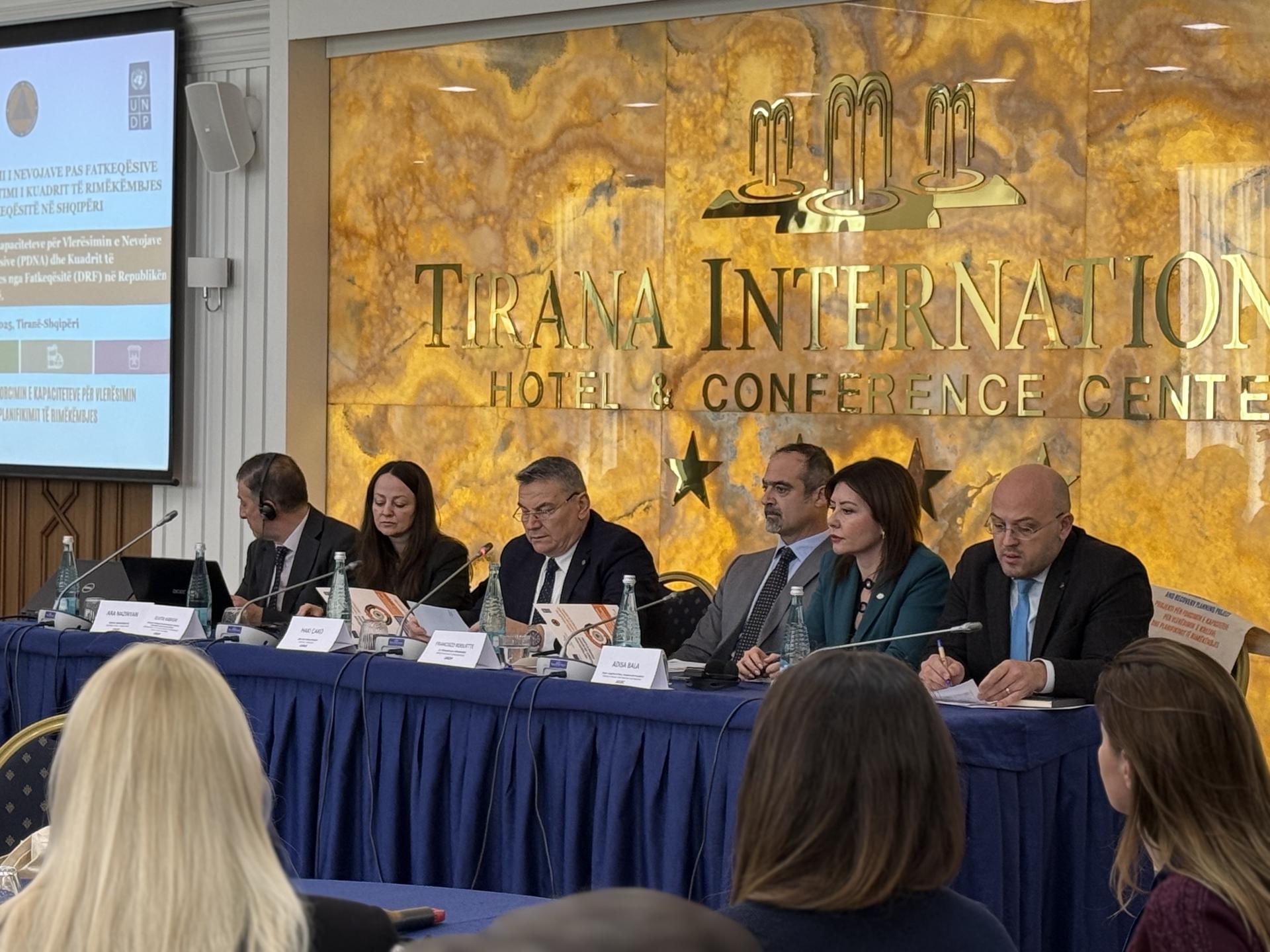 Panel discussion with six speakers at a conference table in front of a decorative backdrop.