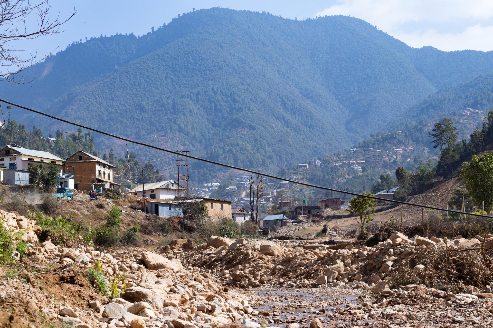 A mountain landscape featuring a bridge connecting two sides, with houses in the foreground.