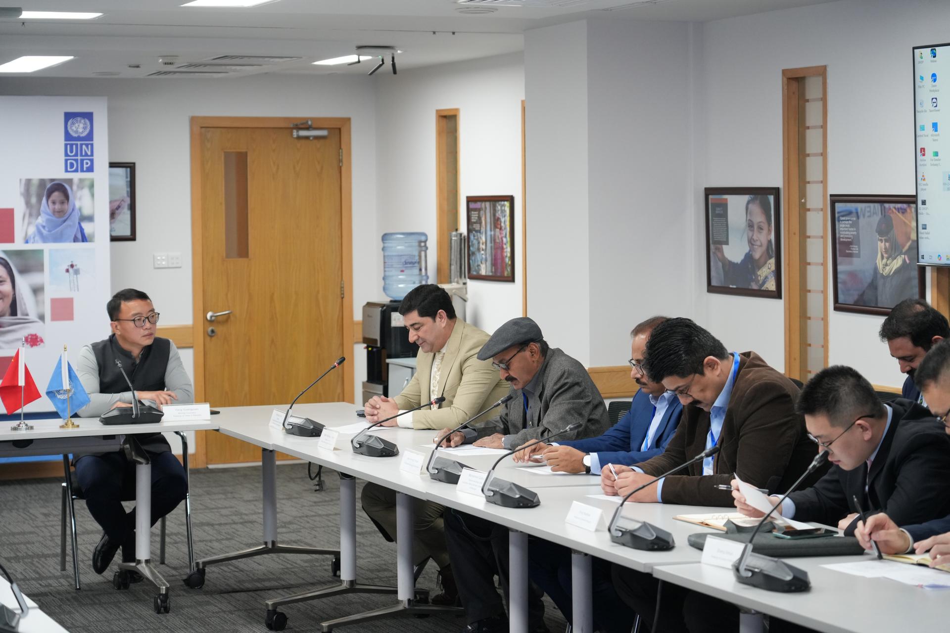 A group of professionals in a meeting room, seated around a long table.