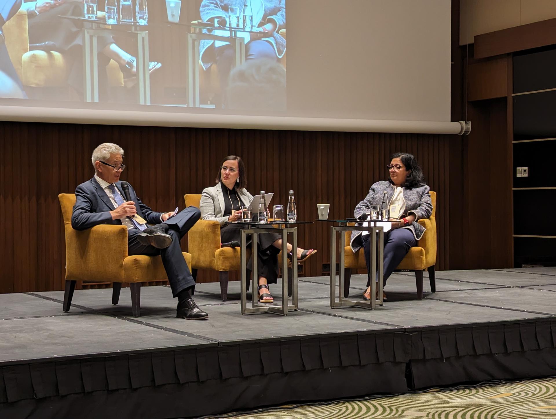 A panel discussion with three speakers seated on stage, engaged in conversation.