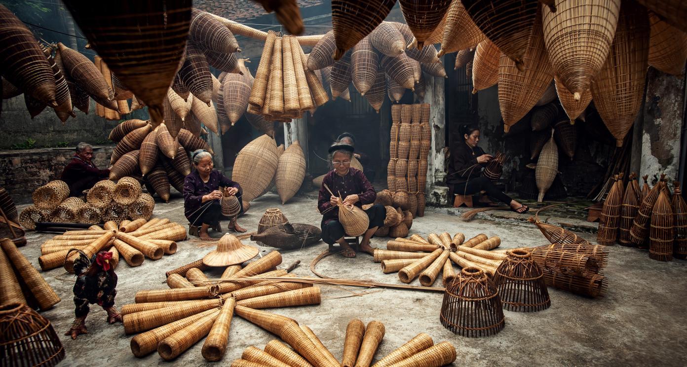 Craftsmen weaving baskets and mats inside a workshop filled with woven materials.
