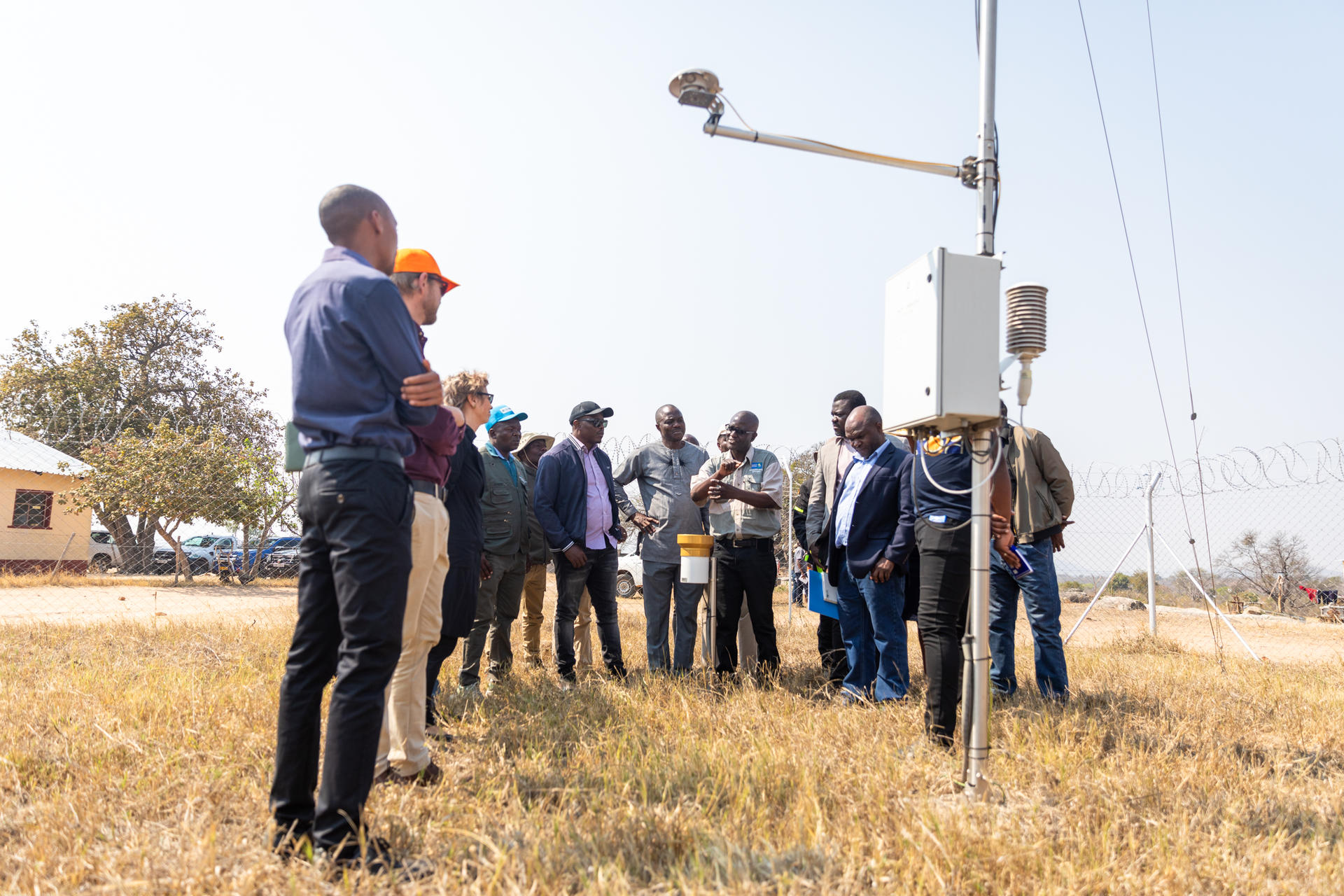 A group of people gathered around a weather station in a grassy field.