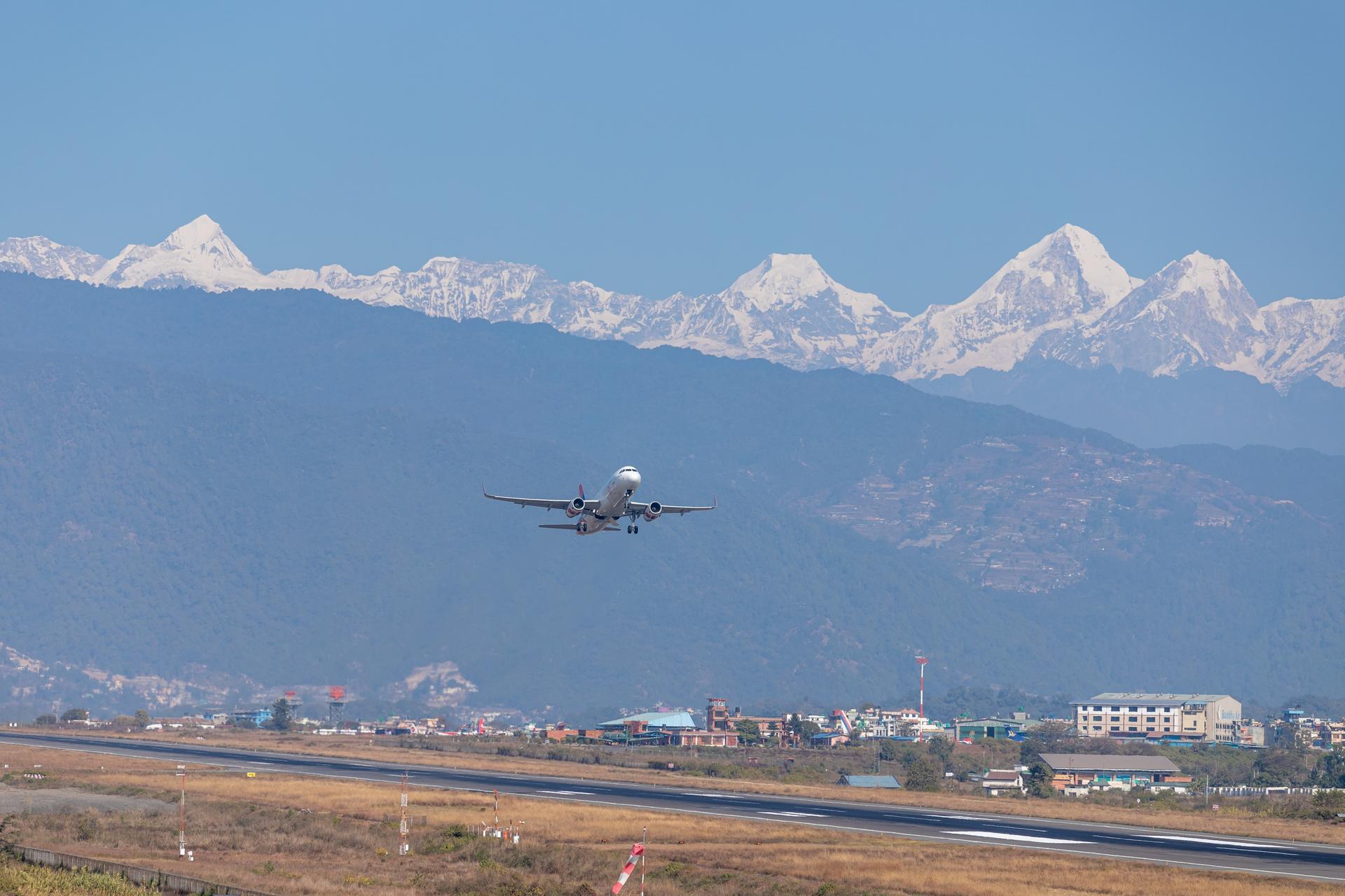 A plane approaches a runway with snow-capped mountains in the background.