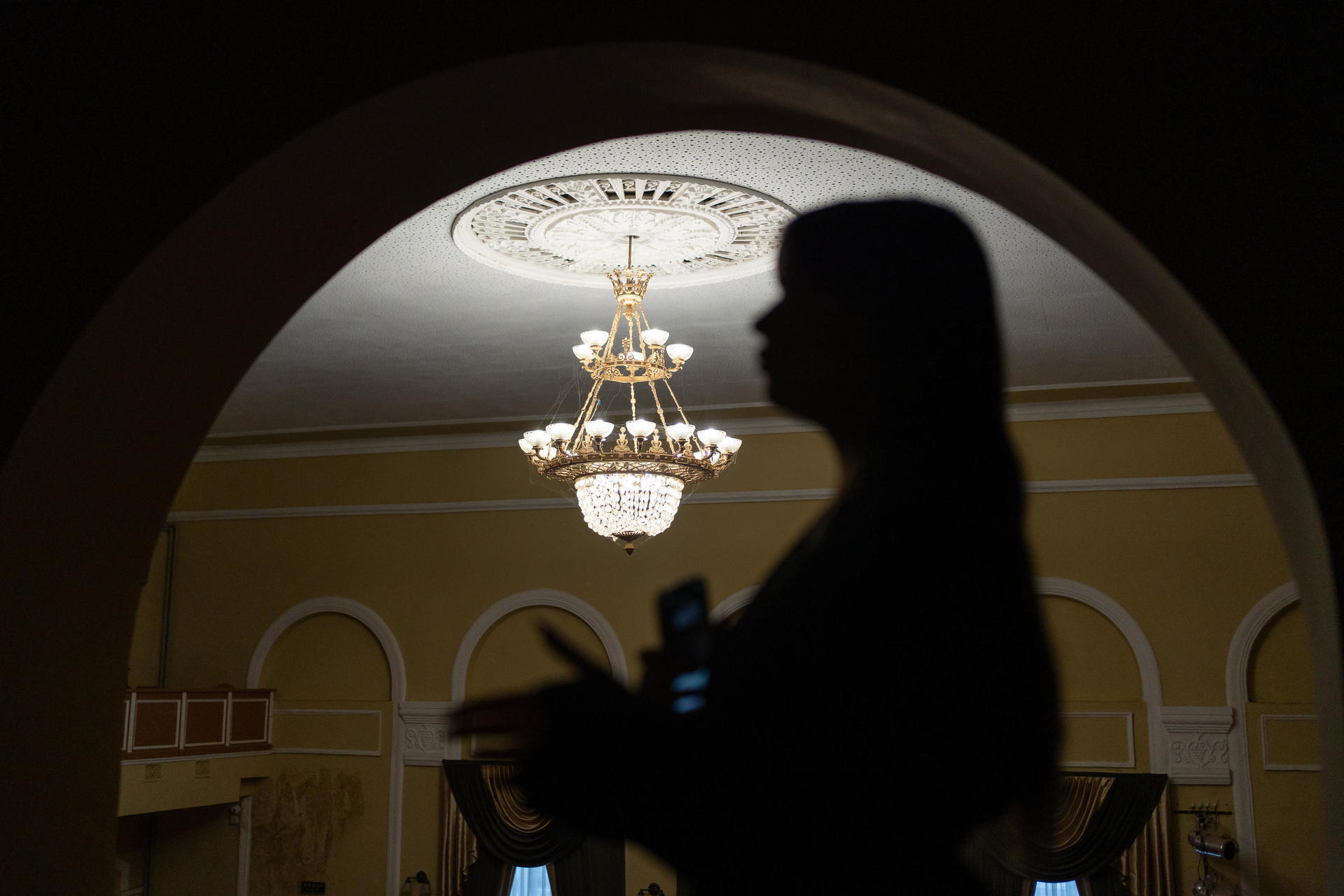 Silhouette of a person against a lit chandelier in an ornate room.