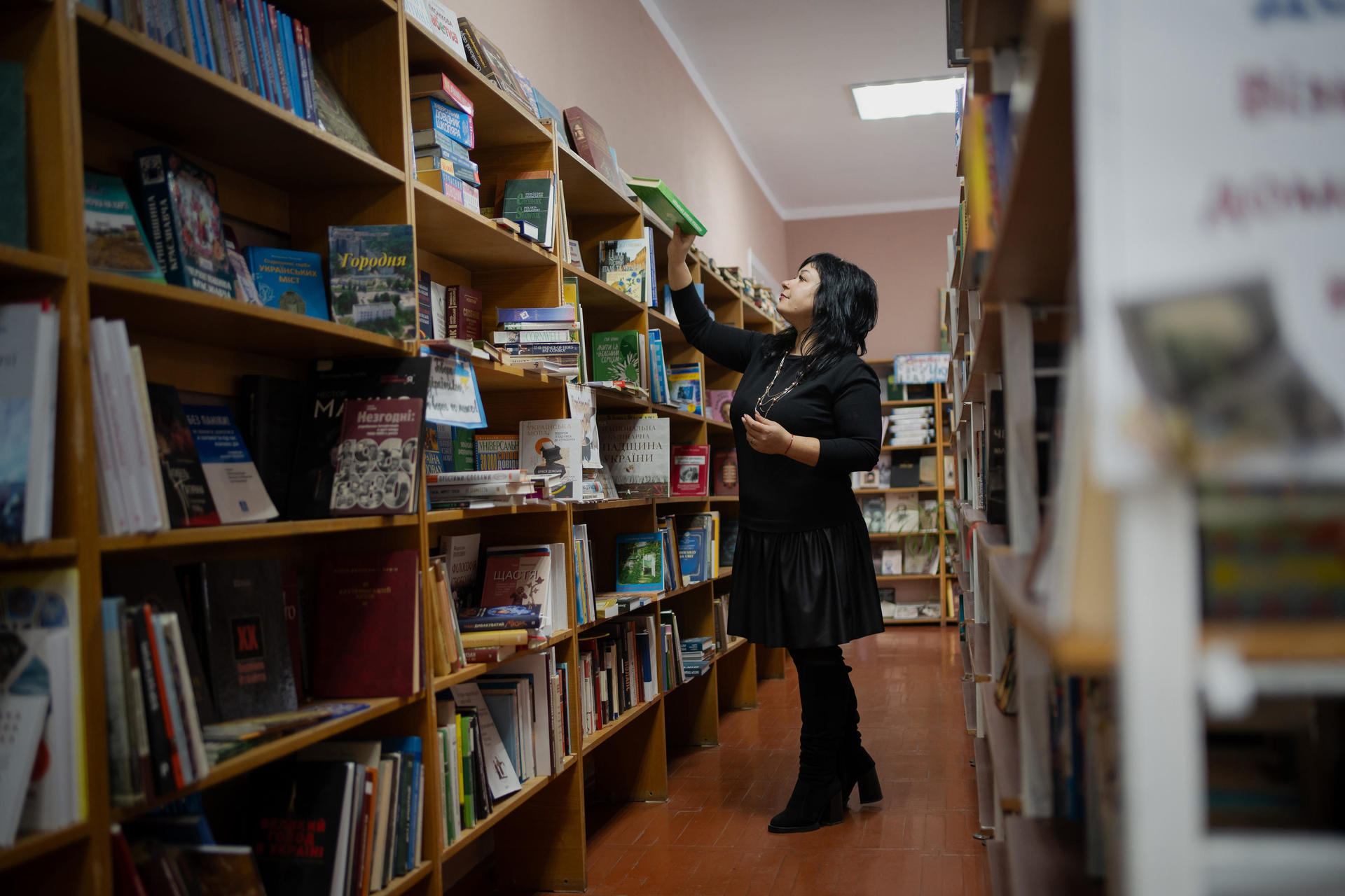 A woman wearing a black dress selects a book from a shelf in a library.