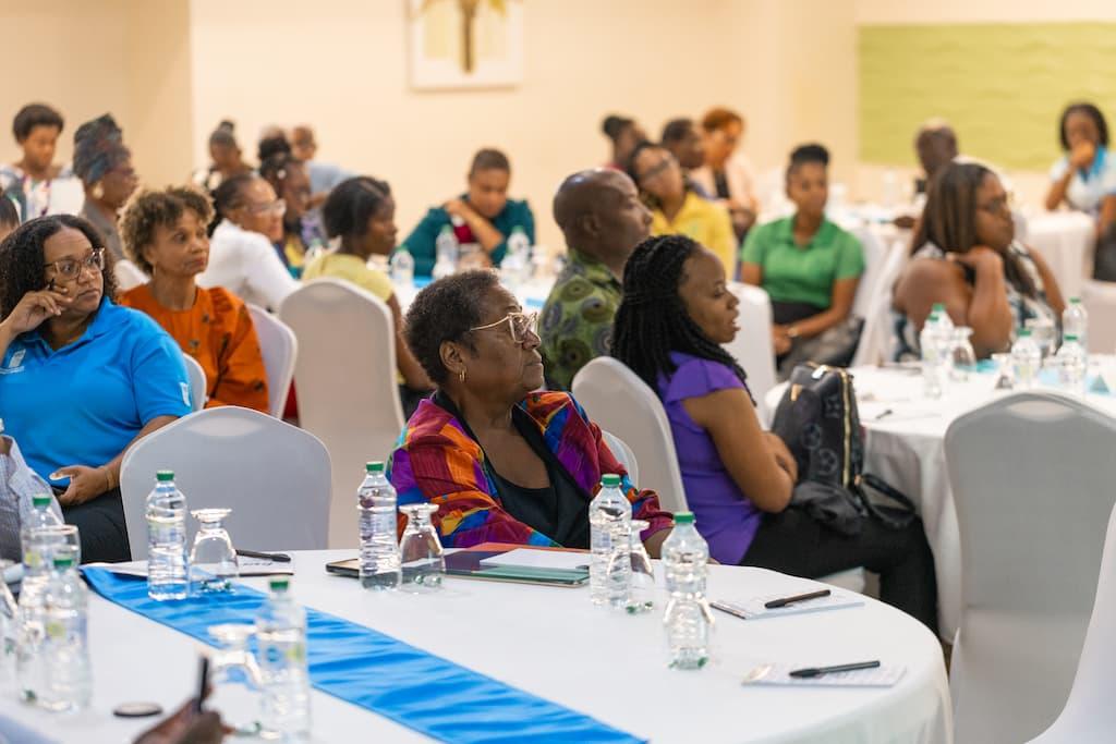 A diverse group of people seated at tables in a conference setting, attentively listening.