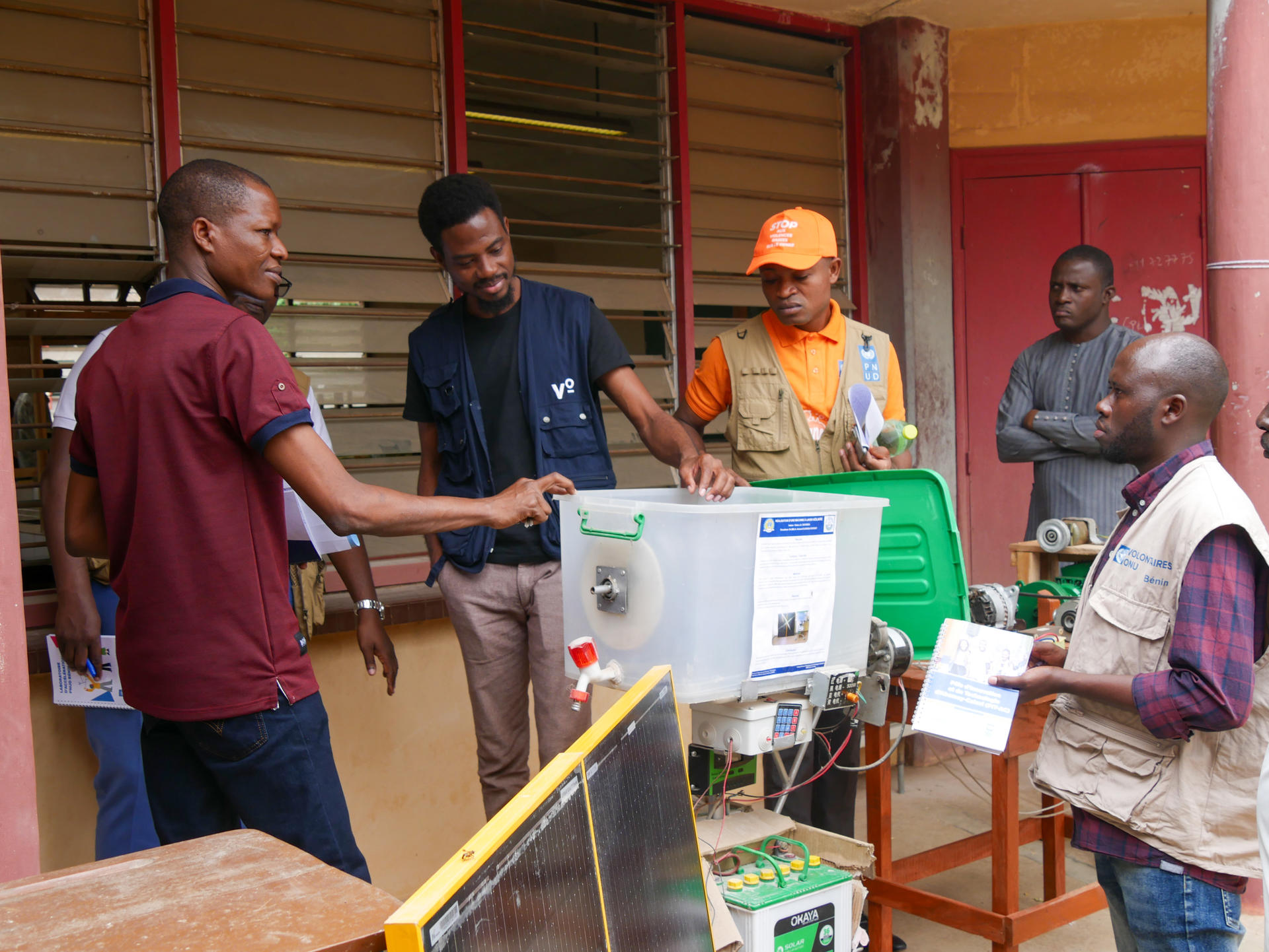 Five men gathered around a green machine in a classroom, discussing its features.