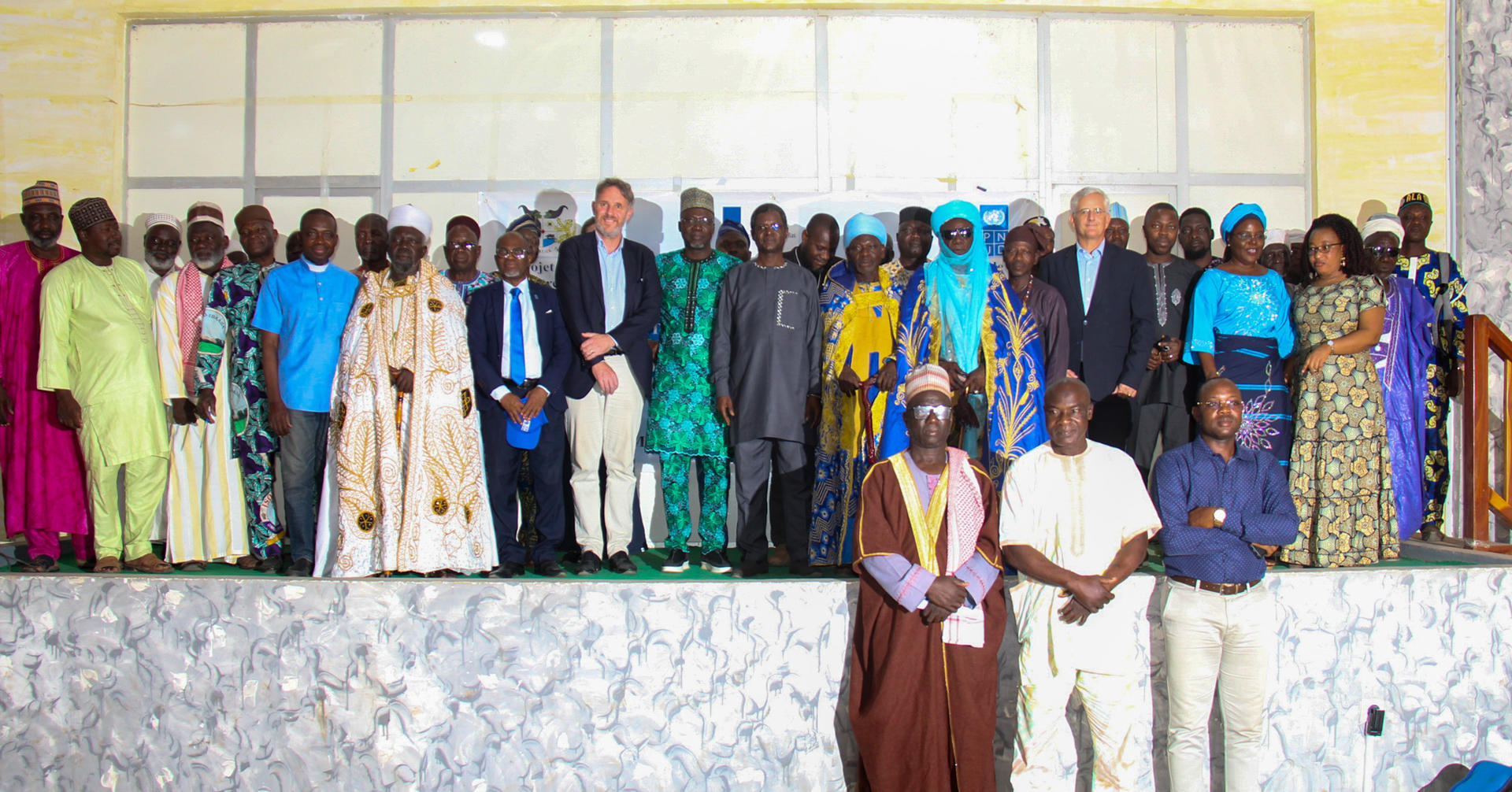 Group photo of diverse individuals in colorful attire, posed on a stage.