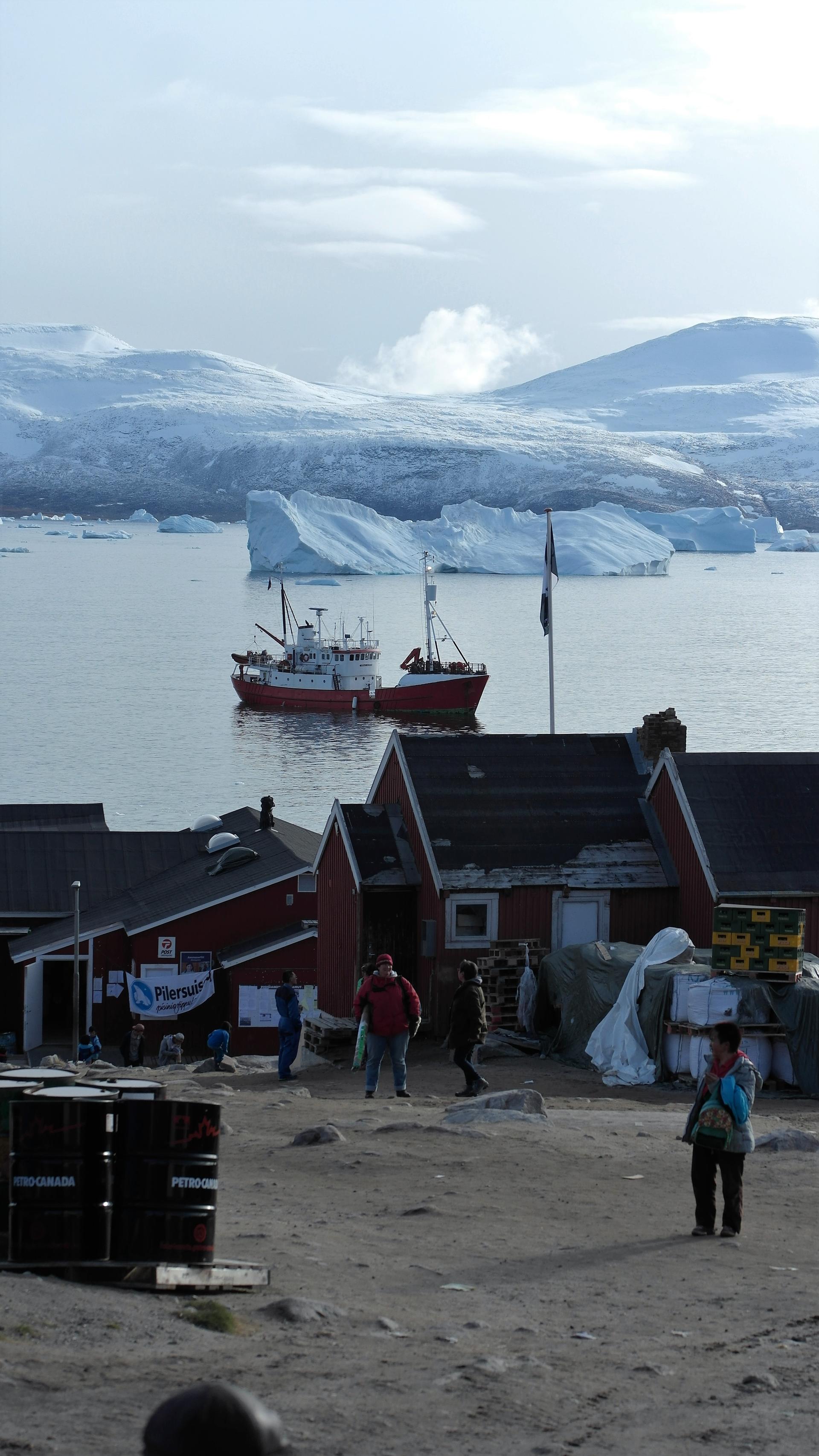 Fishing boat in icy waters, surrounded by mountains and colorful buildings.