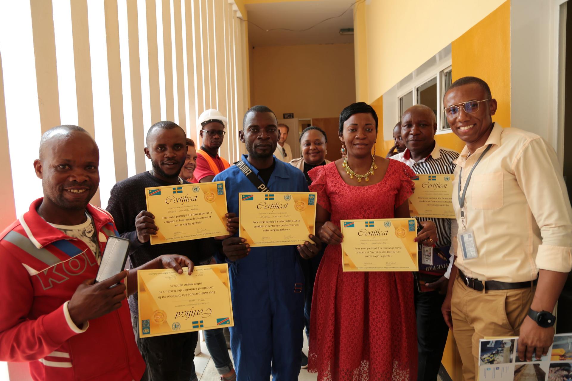 Group of people holding certificates, smiling, in a brightly lit indoor space.