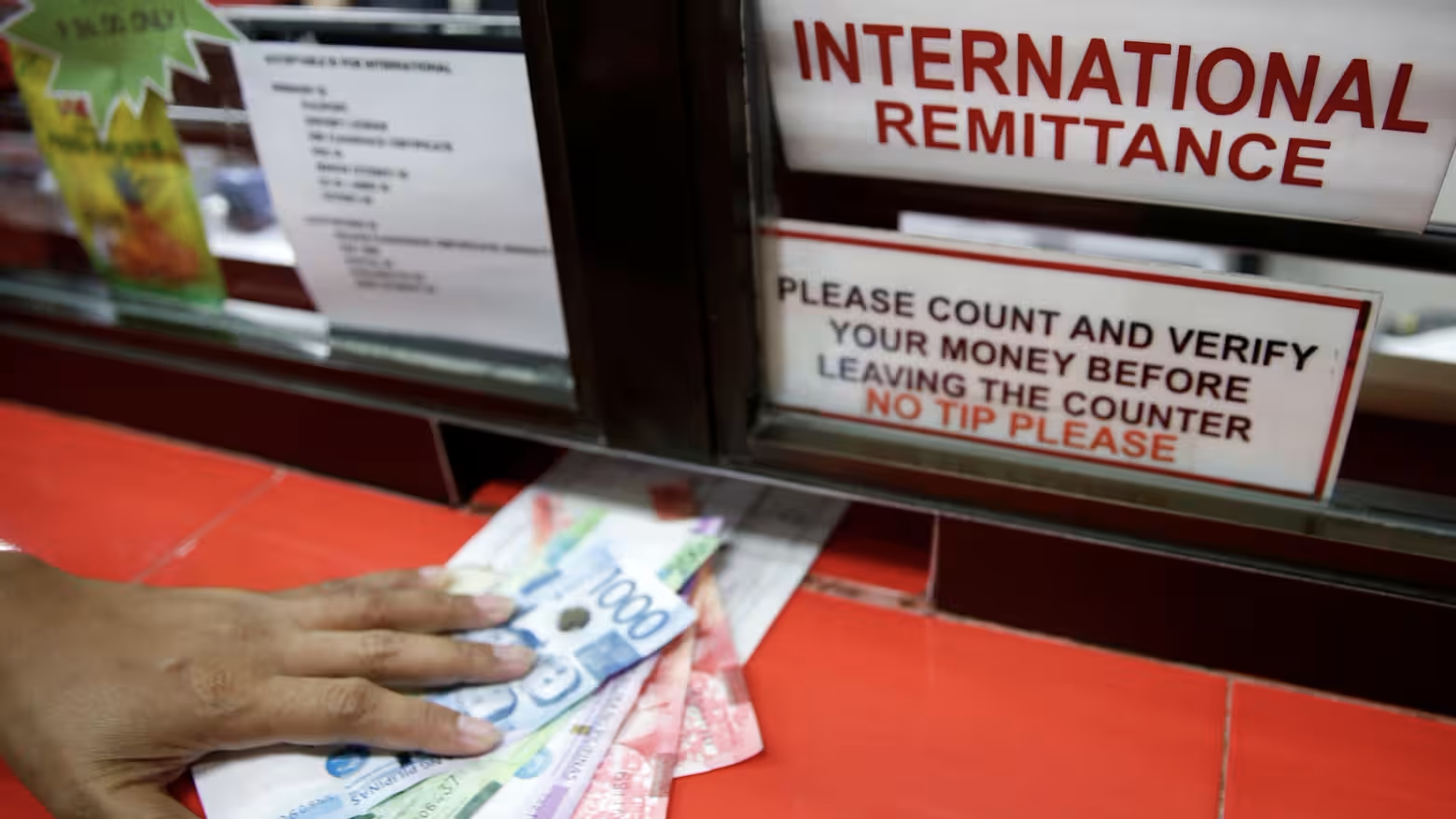 A hand places cash on a counter near a sign for international remittance services.