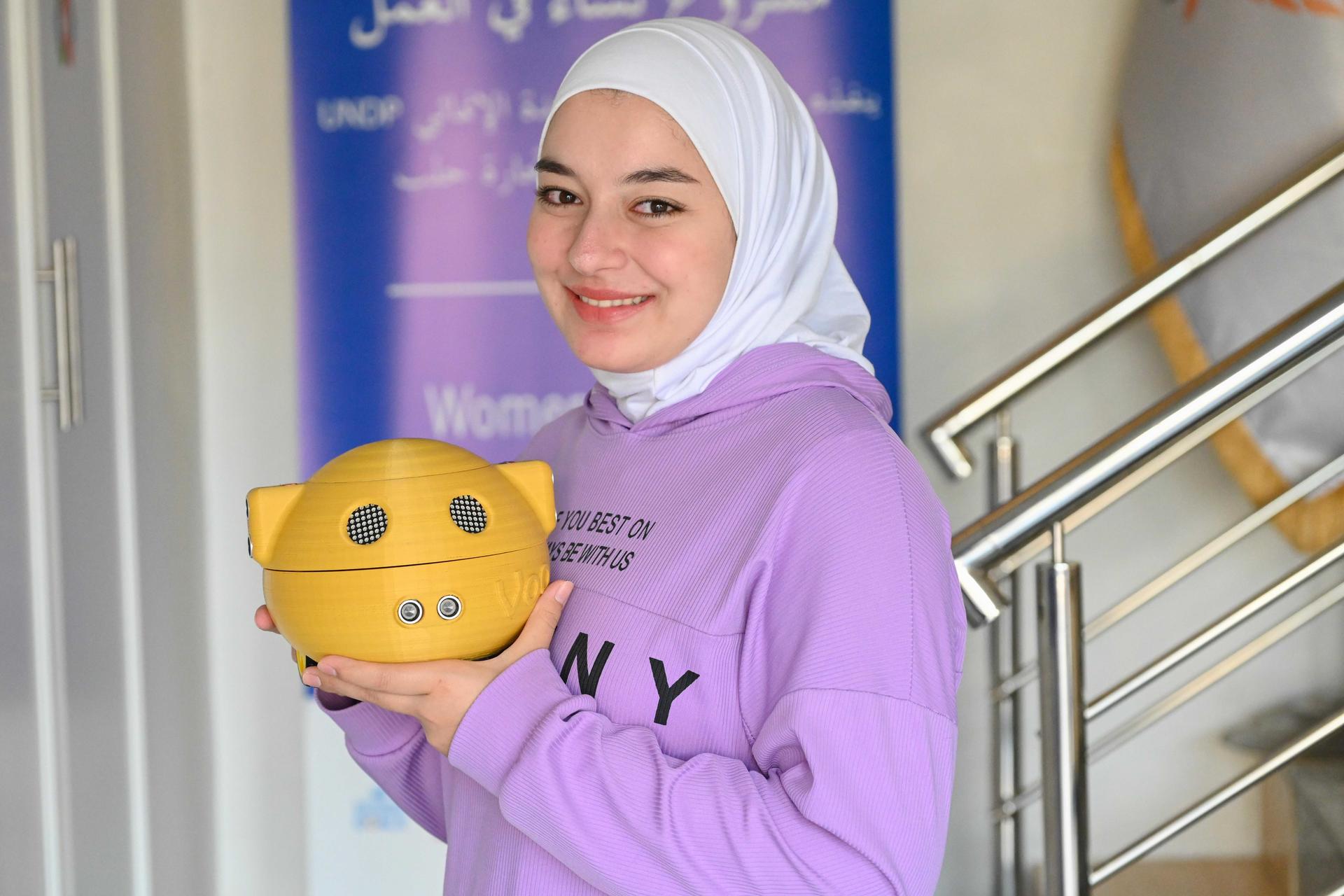 A smiling young woman in a purple hoodie holds a yellow piggy bank.