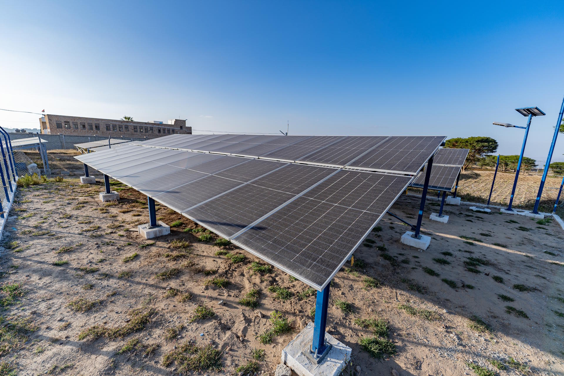 Solar panels arranged on a sandy area with a clear blue sky in the background.