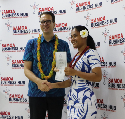 Two people shaking hands at a business event, with a banner reading "Samoa Business Hub" in the background.