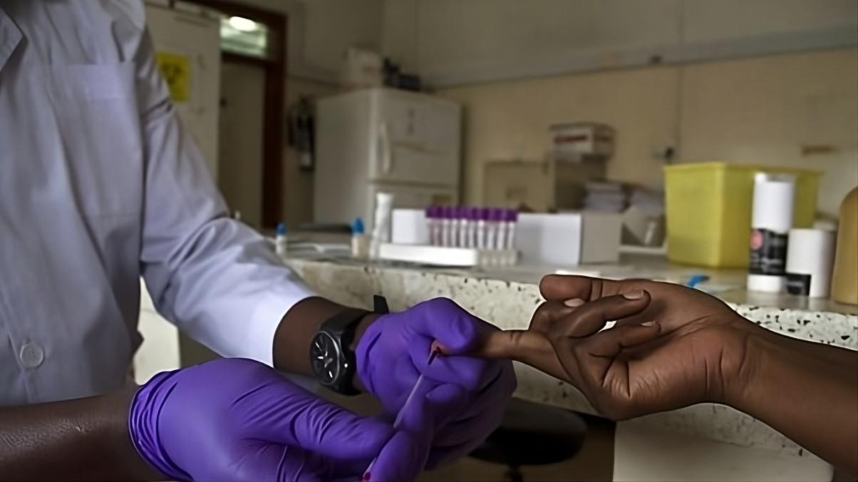 A healthcare worker in gloves draws blood from a patient's finger in a lab setting.