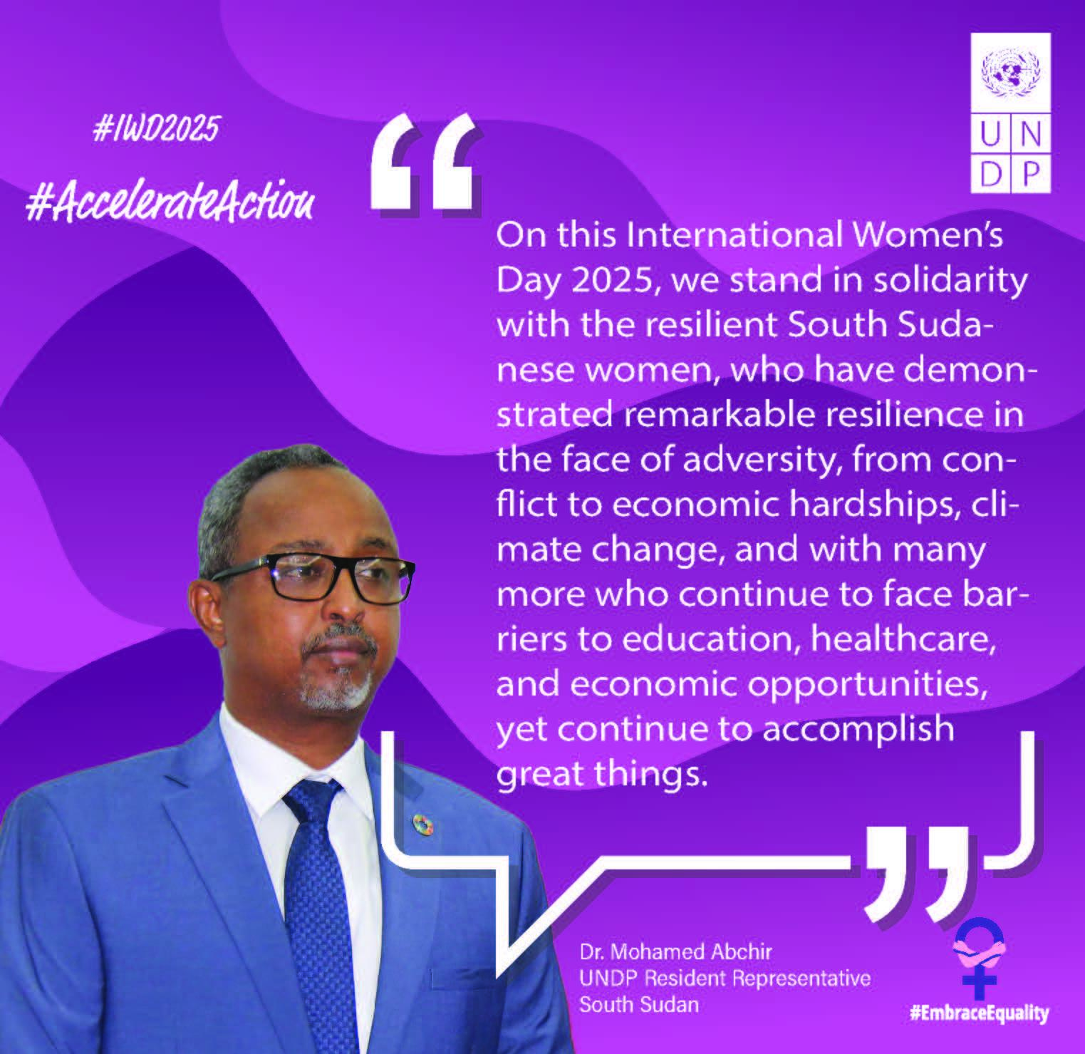 Man in glasses and a suit speaking, with text about International Women’s Day 2025 in the background.