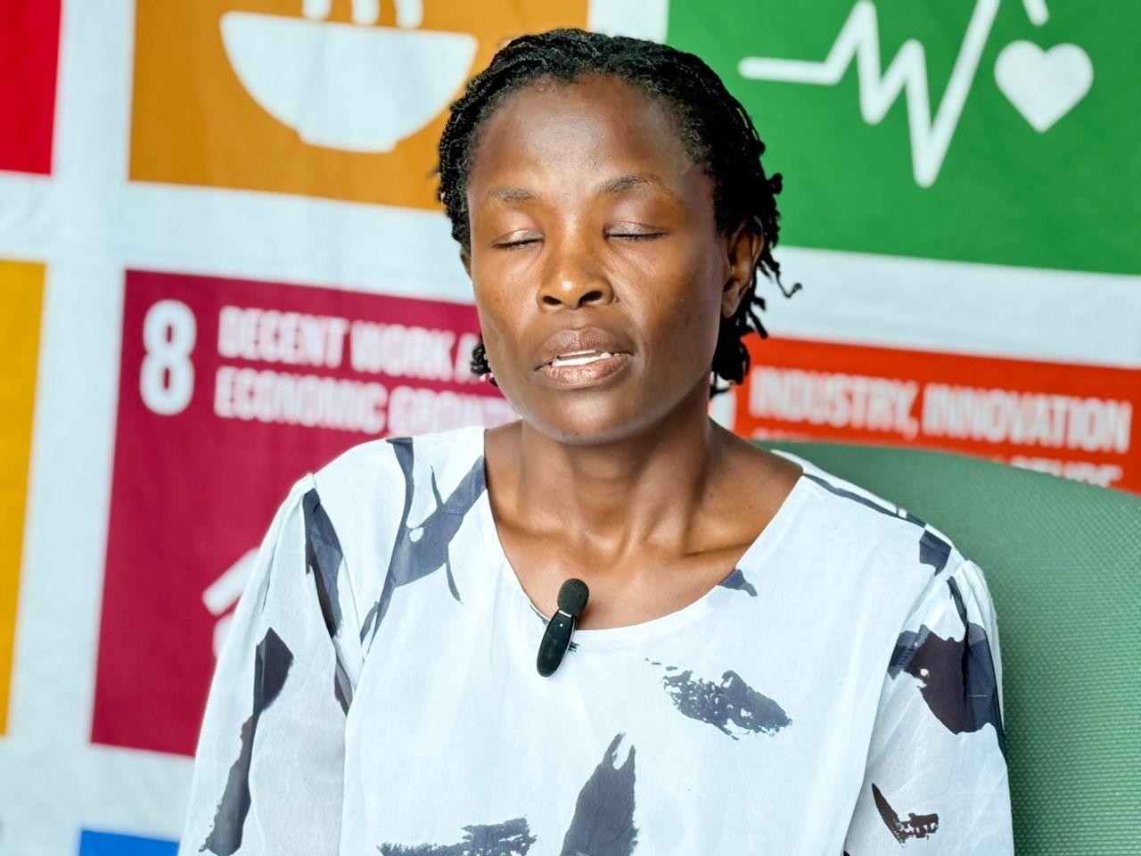 A woman with closed eyes sits in front of colorful sustainability-related banners.