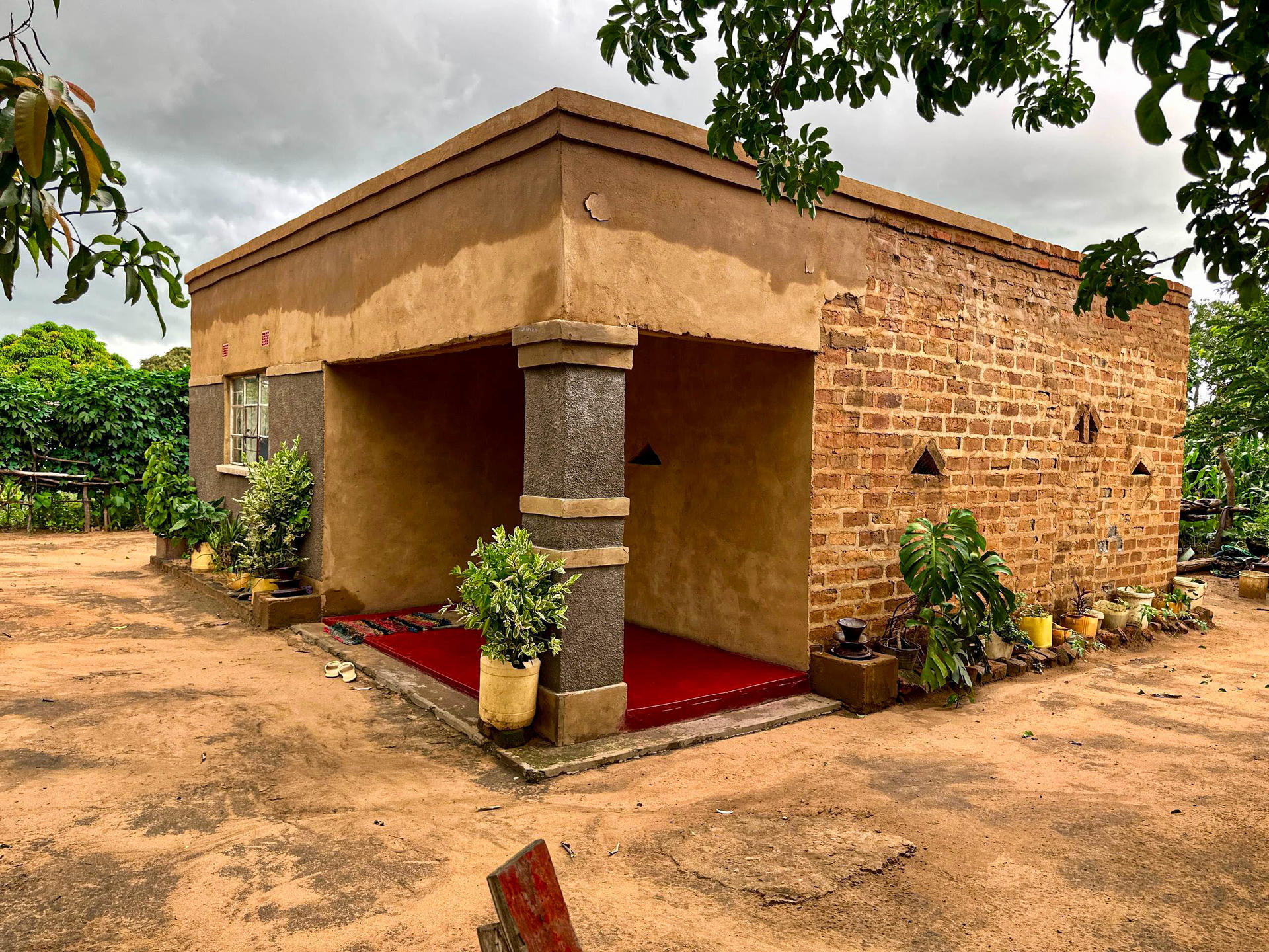 Single-story building with a brick exterior, red carpet, and potted plants in a cloudy setting.