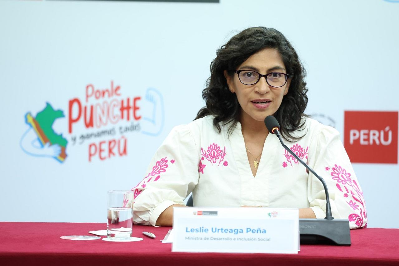 Woman with glasses wearing a white blouse speaks at a conference table.