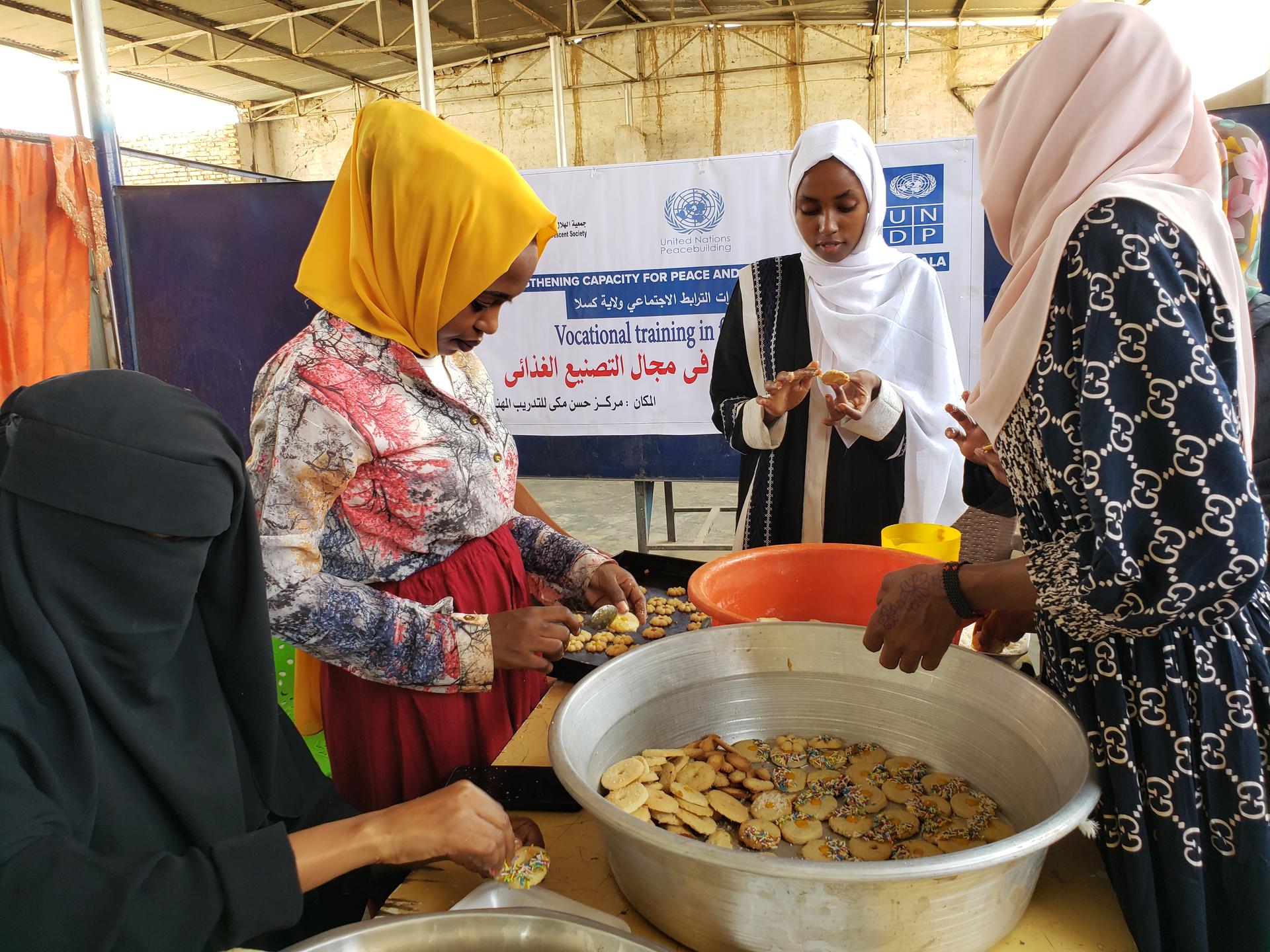 Women in colorful attire preparing snacks in a communal setting, smiling and engaged.