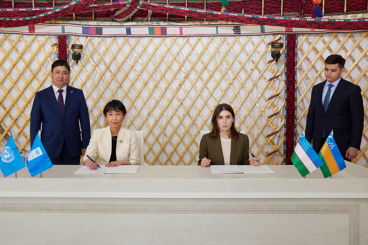 Four delegates stand around a table with flags, signing an agreement in a yurt.