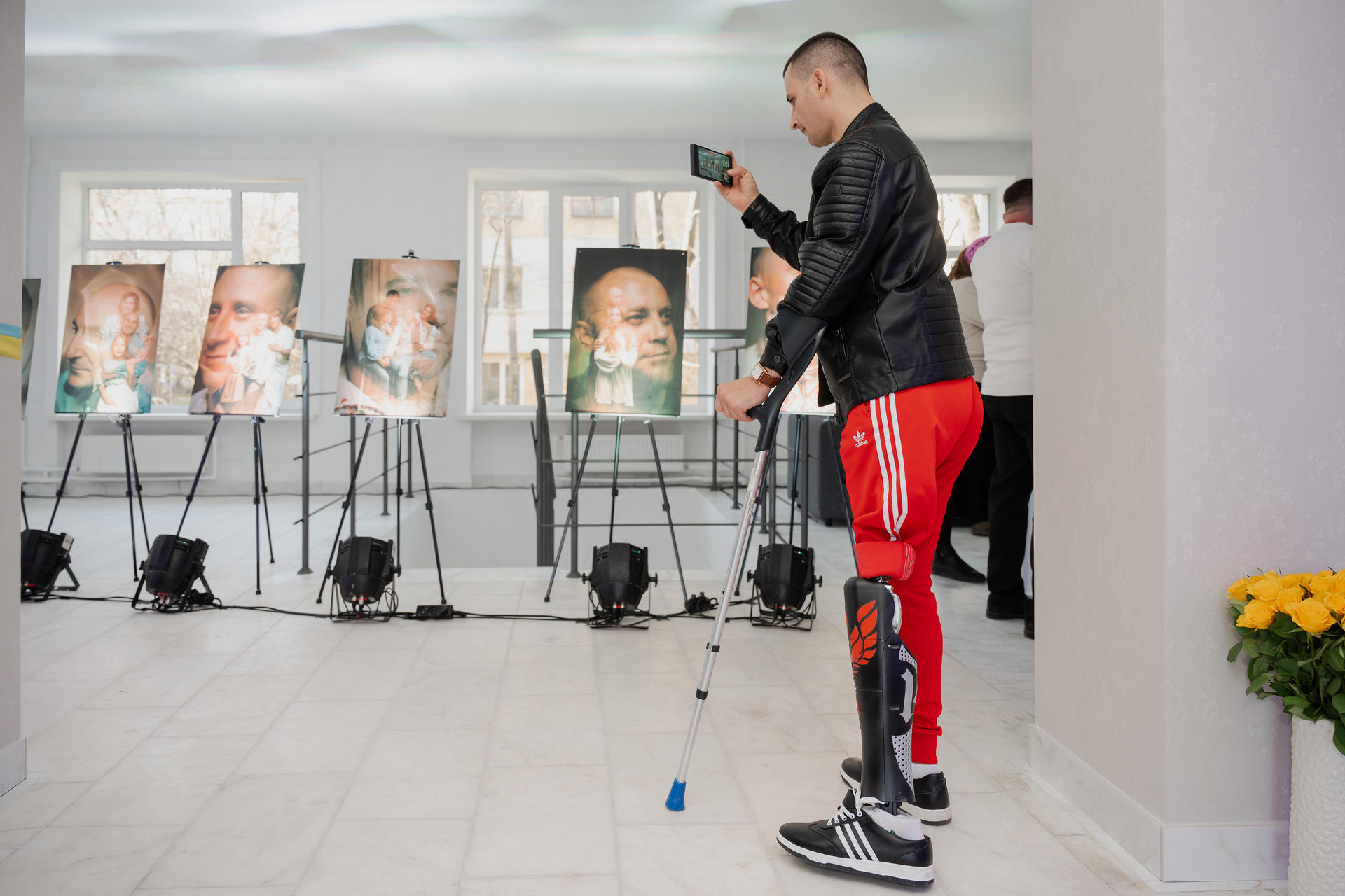 A person using a cane stands in an art gallery, viewing portraits displayed on easels.