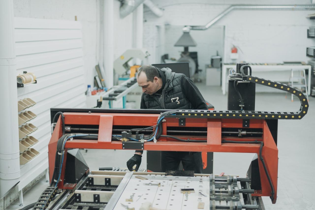 A man operates a large red machine in a workshop, focused on his task.