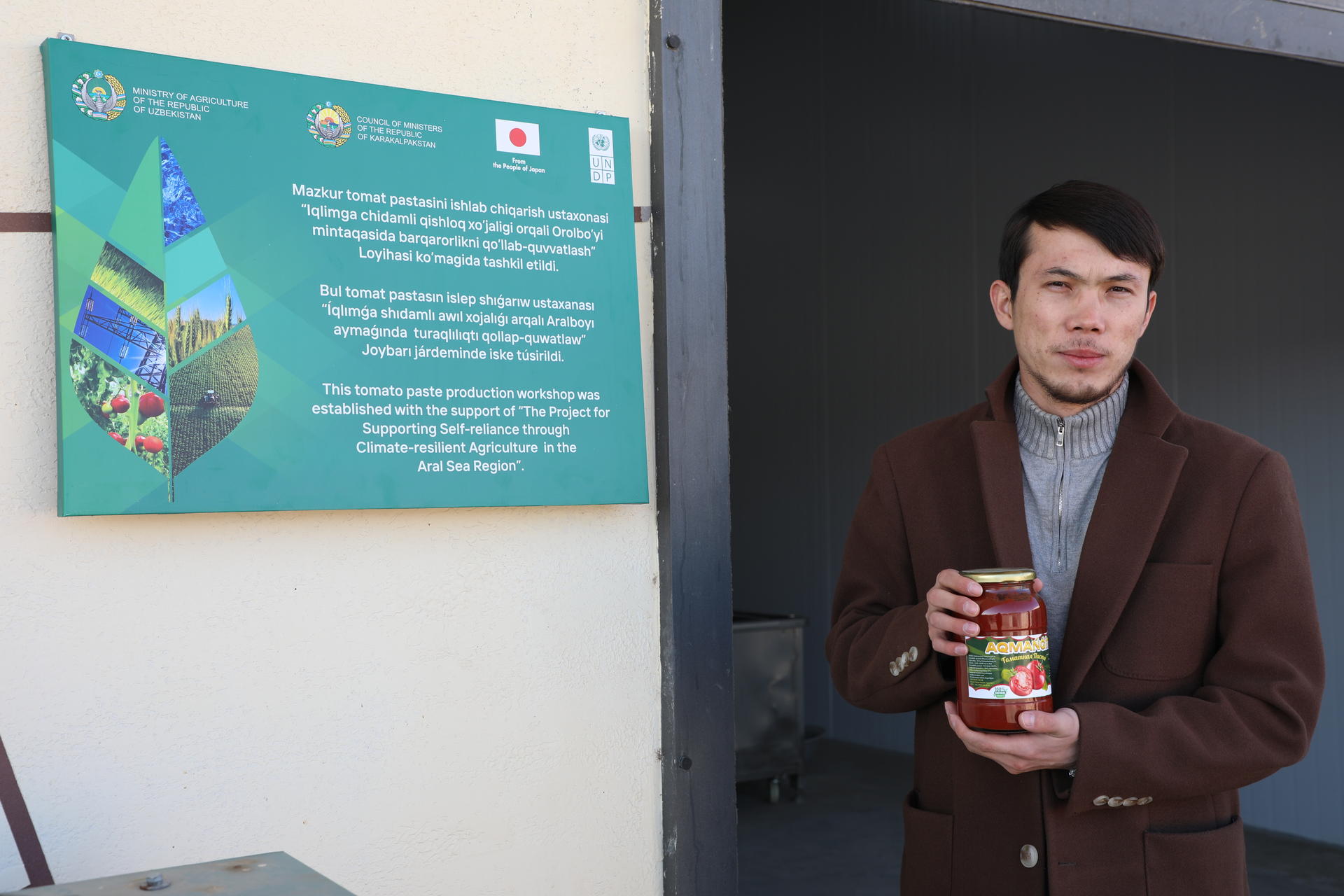 A man holds a can in front of an informational sign on a wall.