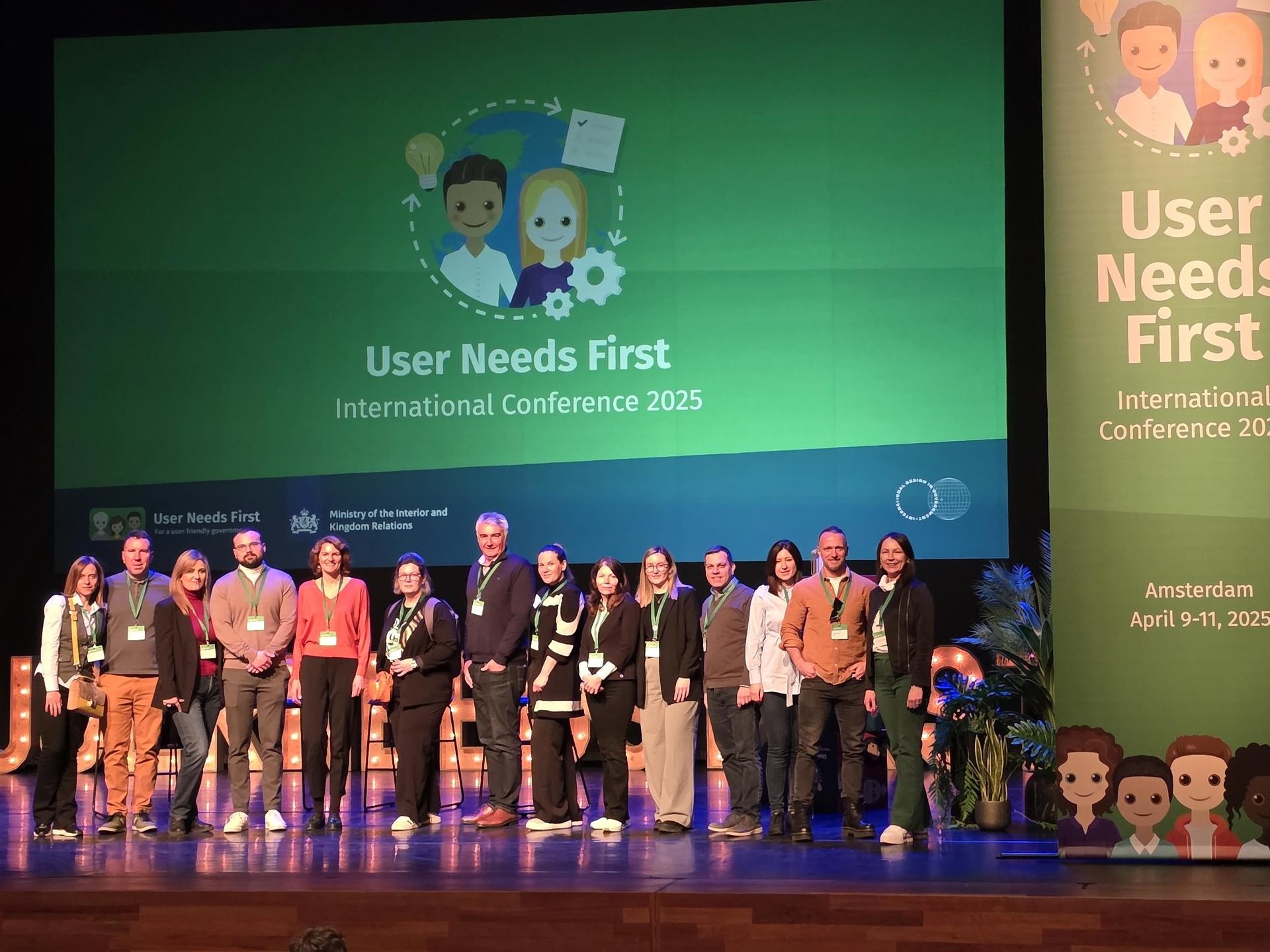A diverse group of people stands on stage in front of a presentation backdrop at a conference.