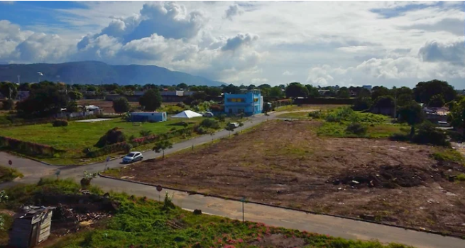 Open landscape with a blue building, roads, and scattered greenery under a cloudy sky.