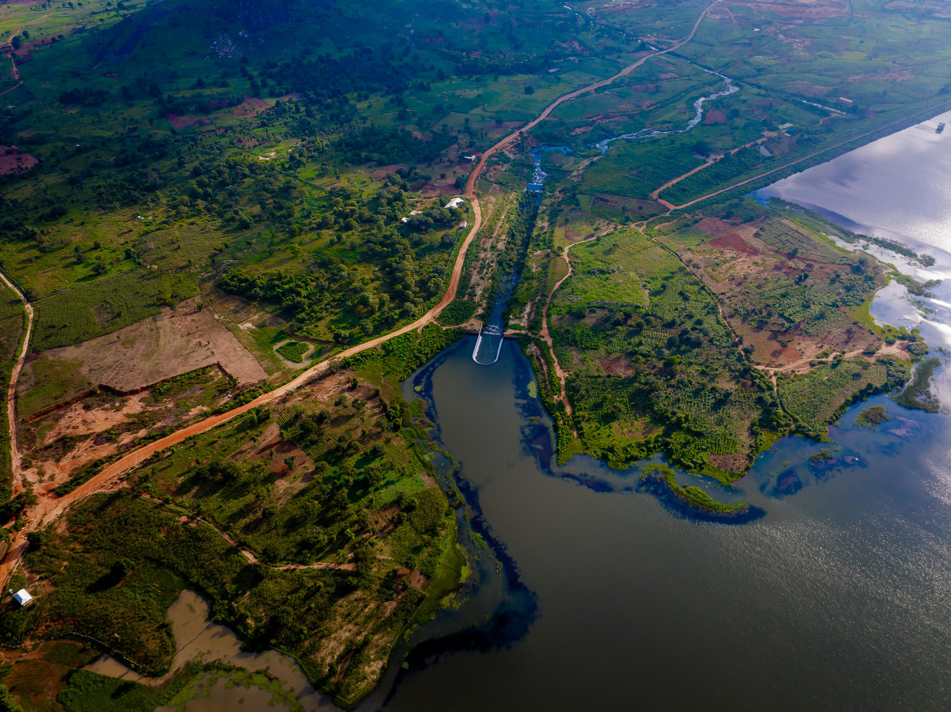 Aerial view of lush green landscape with winding roads and rivers meeting a lake.
