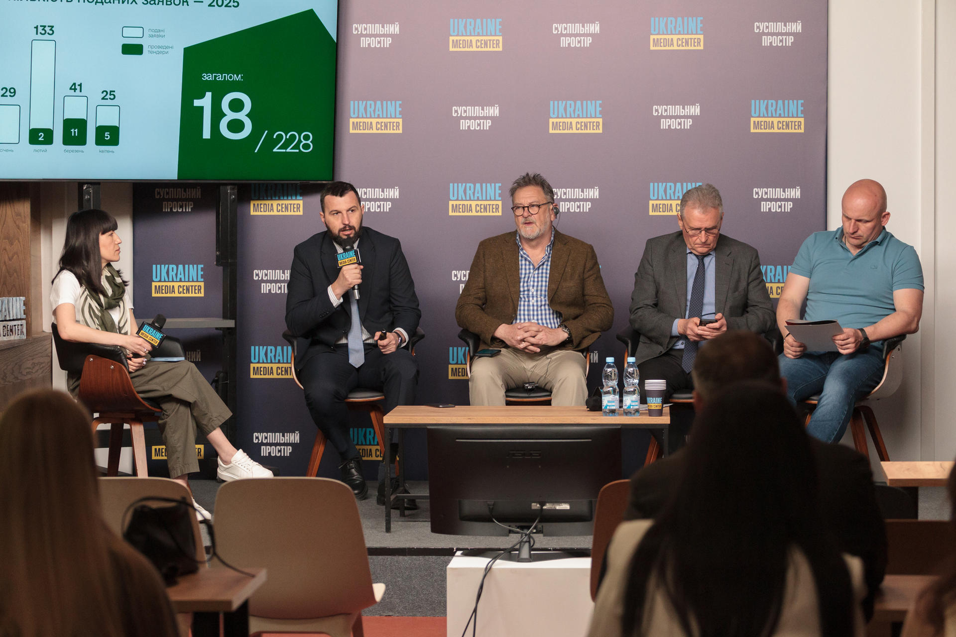 Panel discussion with five speakers and audience in a conference setting.