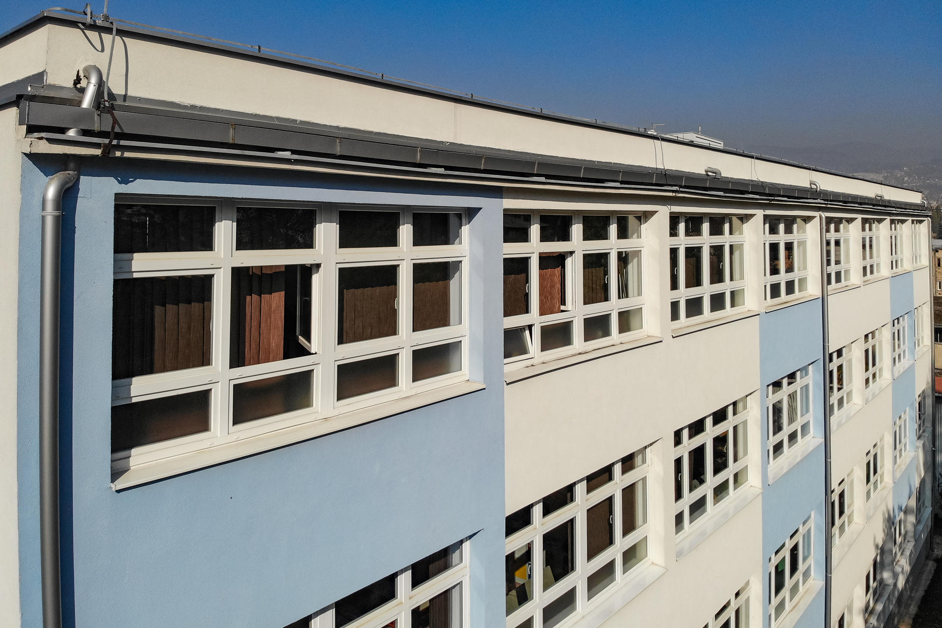 Corner of a blue and white building with multiple windows under a clear blue sky.
