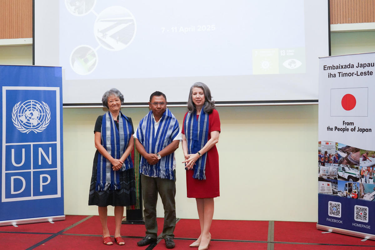 Three individuals stand on a stage, wearing blue and white striped scarves.
