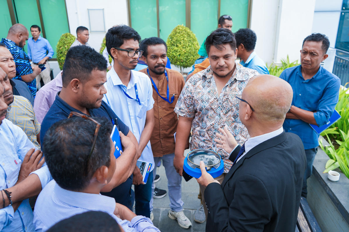 A group of people gather around a speaker presenting an item outdoors.