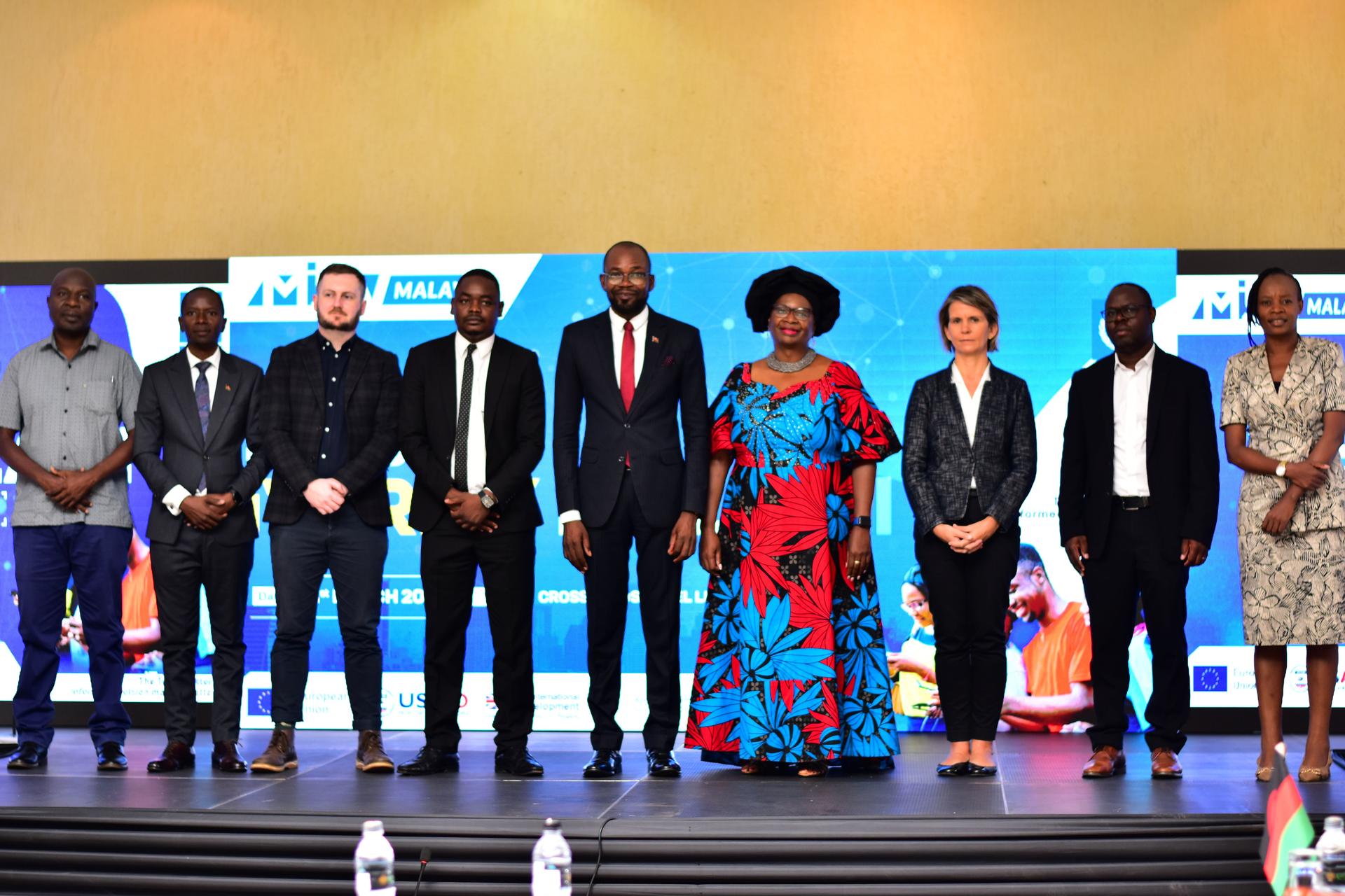 A group of nine dressed professionals stands on stage, smiling at the camera.