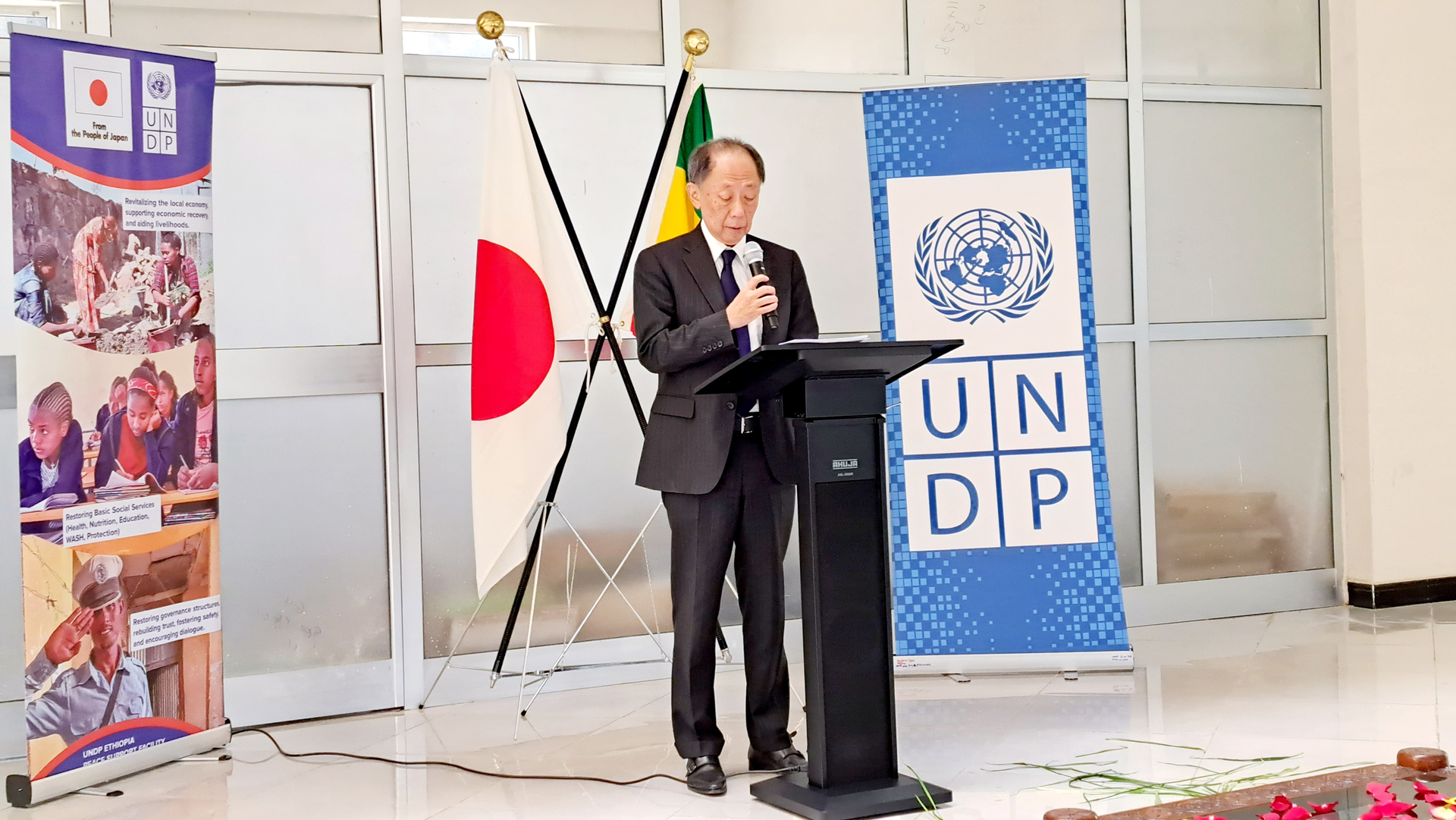A man speaking at a podium with flags behind him at a conference event.