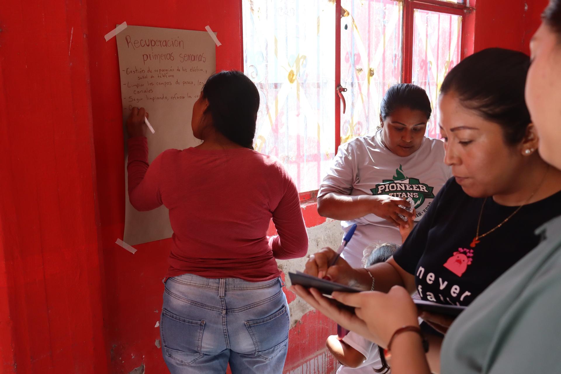 Three people engaged in activities in a brightly colored red room. One writes on a board, while two others use smartphones.