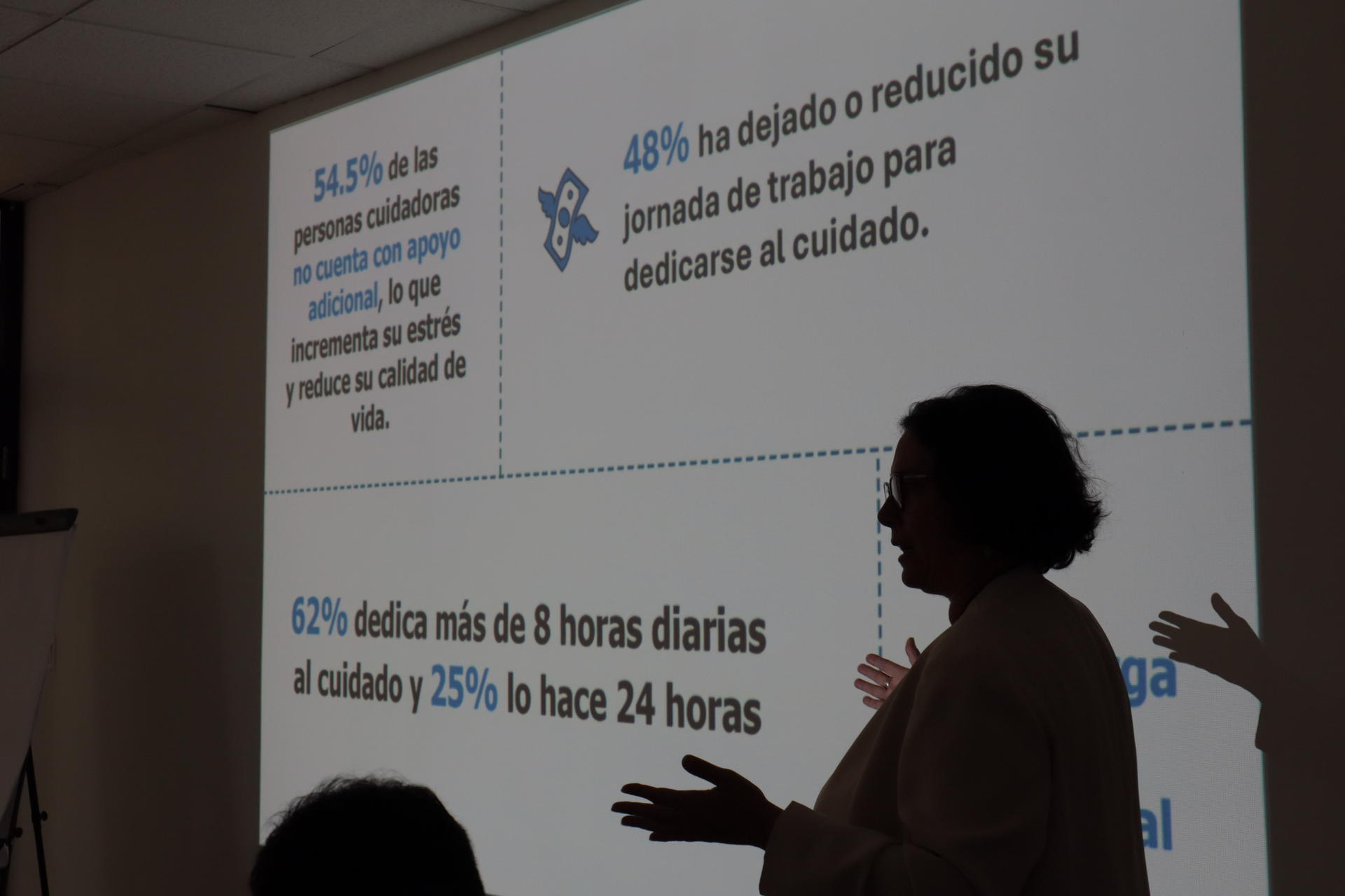 A silhouetted presenter gestures while statistics are projected on a screen.