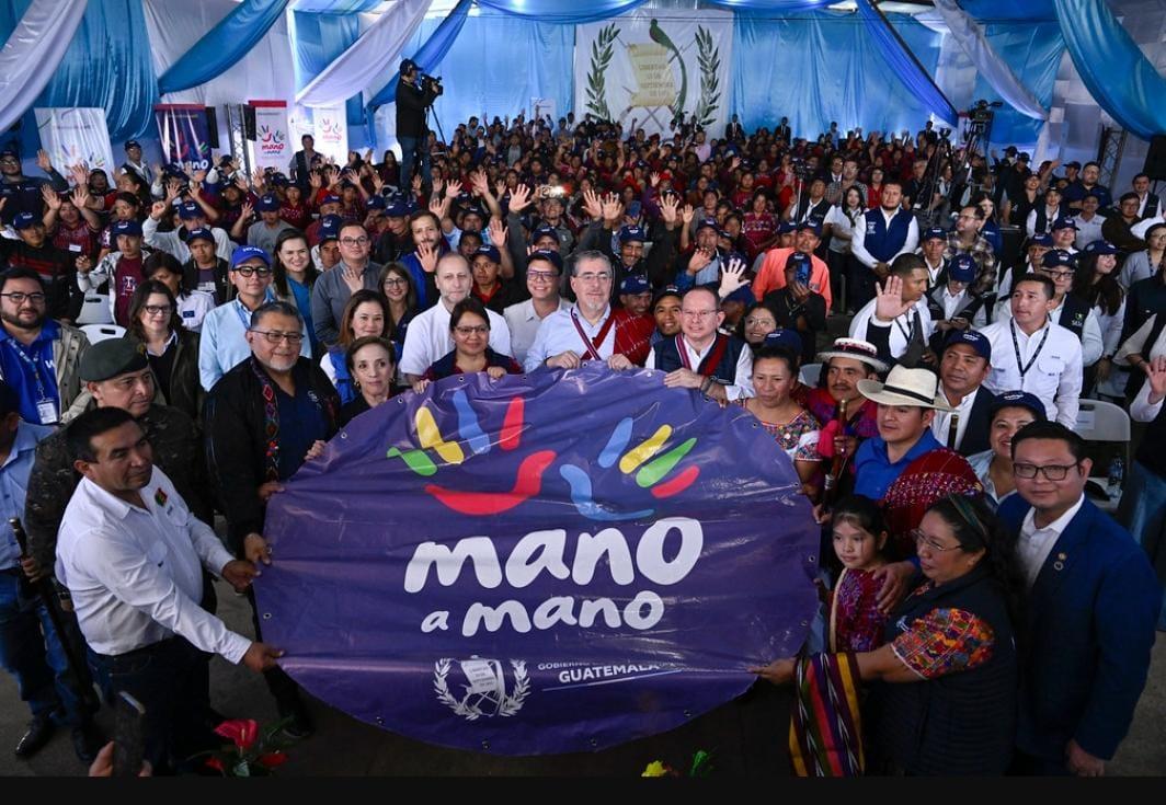A large group of people holding a colorful banner in a festive indoor setting.