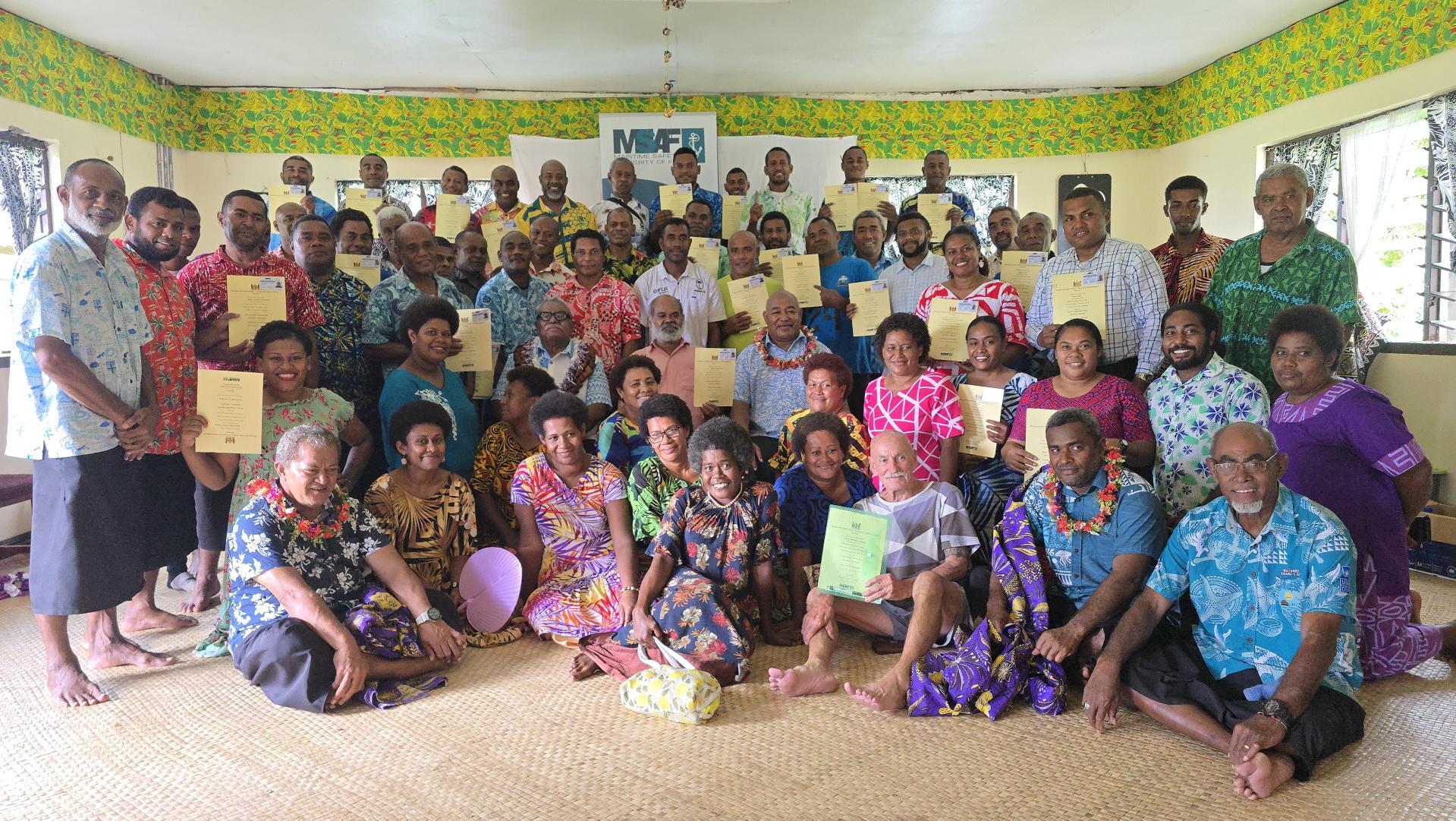 A large group of diverse individuals, smiling and holding certificates, in a colorful room.