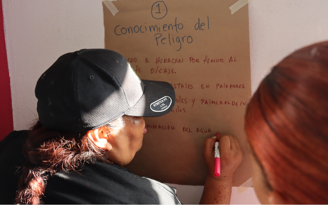 A person wearing a black hat writes on a large brown paper with notes.