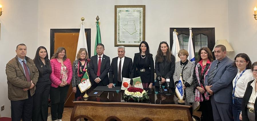 A diverse group of professionals poses together in an office setting, several flags displayed.