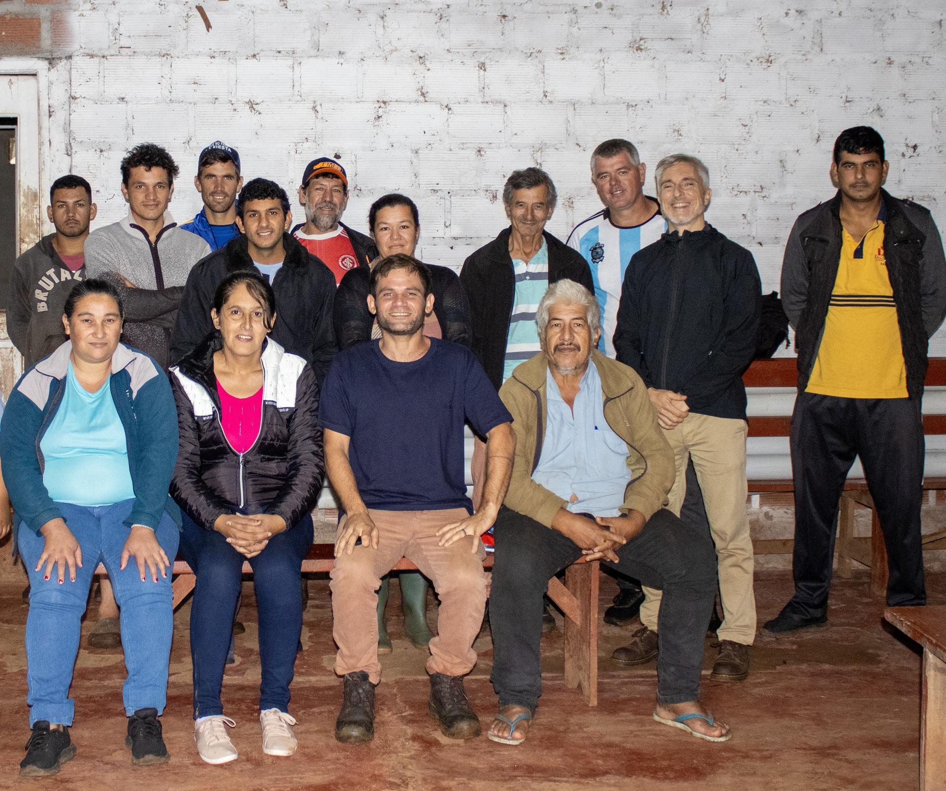 Una foto grupal con 15 personas, sonriendo, con un fondo de ladrillos blancos.