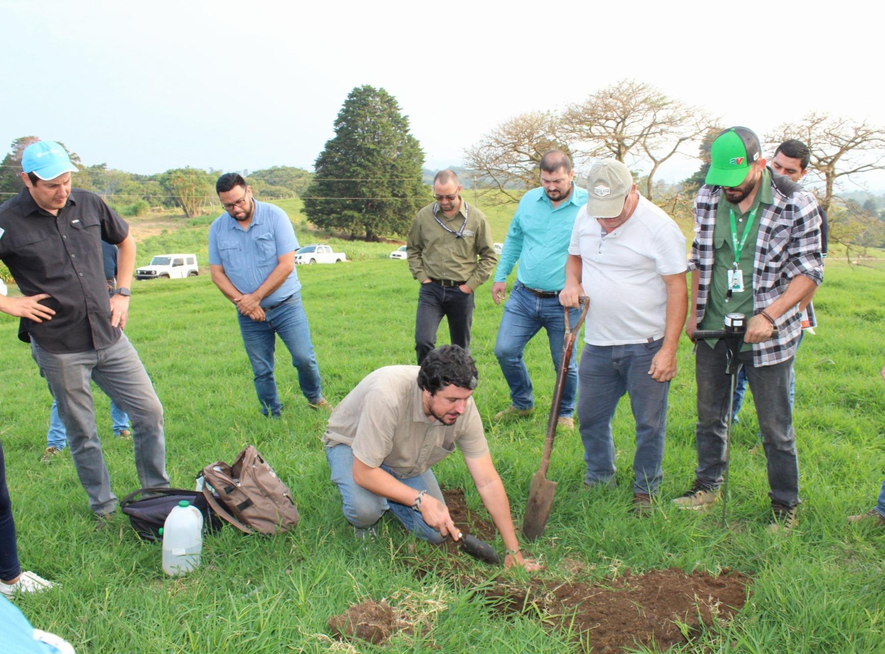 A group of people watches as a man digs in the soil at an outdoor location.