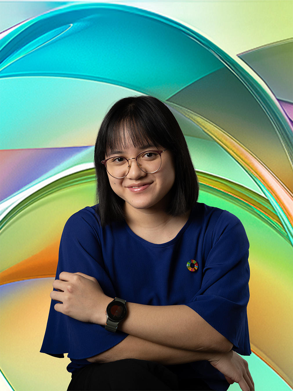 A smiling young woman with glasses stands confidently against a colorful abstract background.