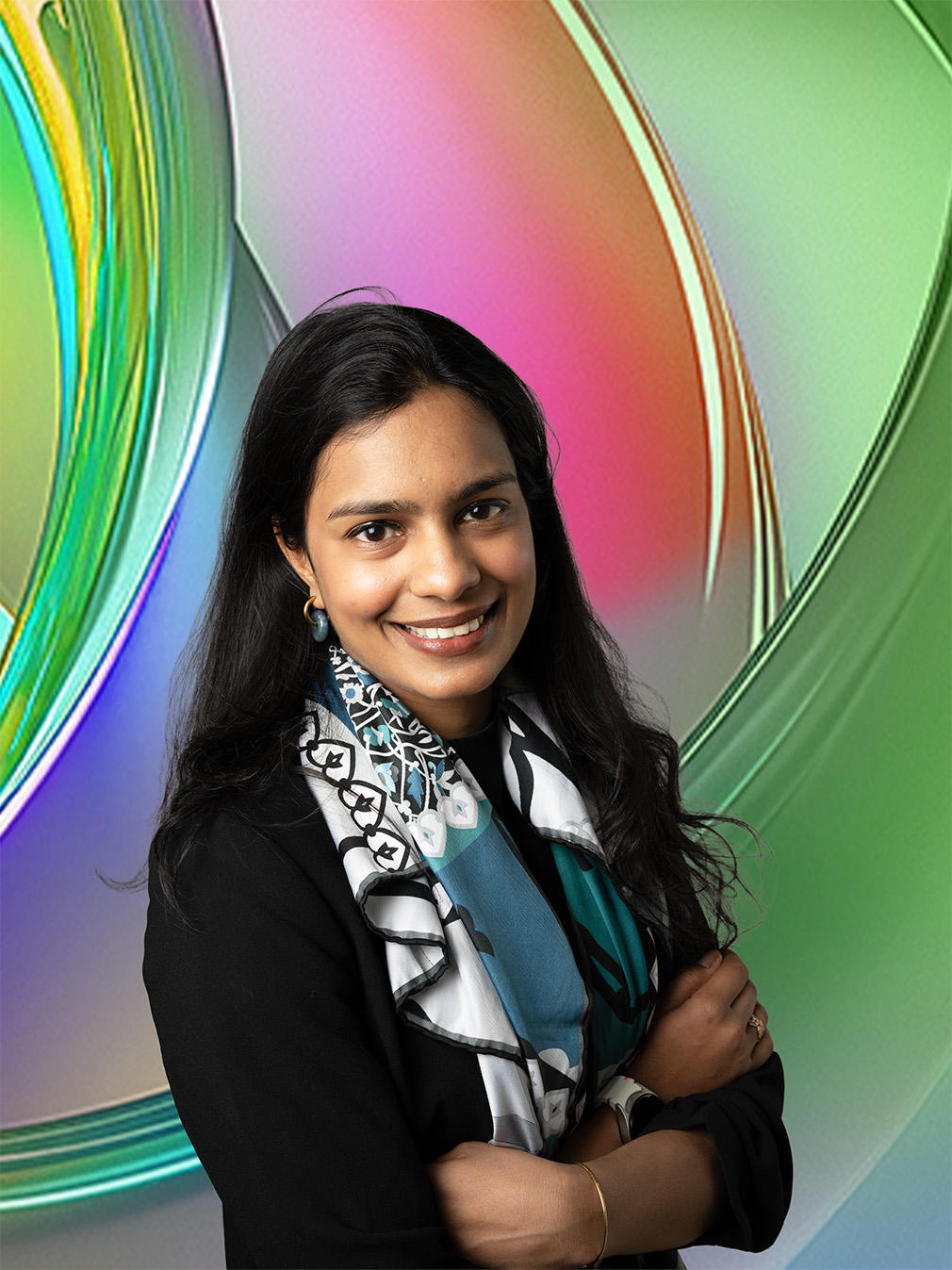 Smiling woman with long dark hair, wearing a black jacket and colorful scarf, against a vibrant background.