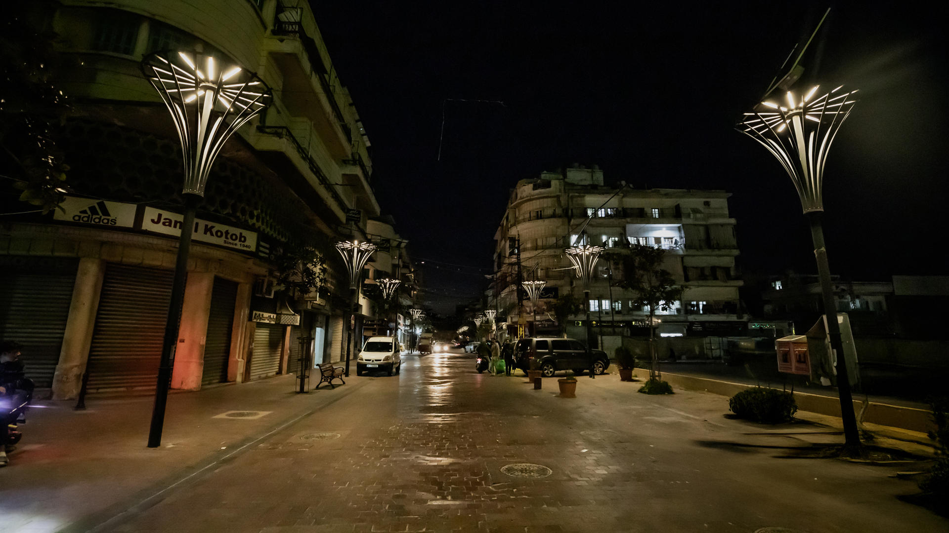 Empty street at night illuminated by decorative street lamps and nearby buildings.