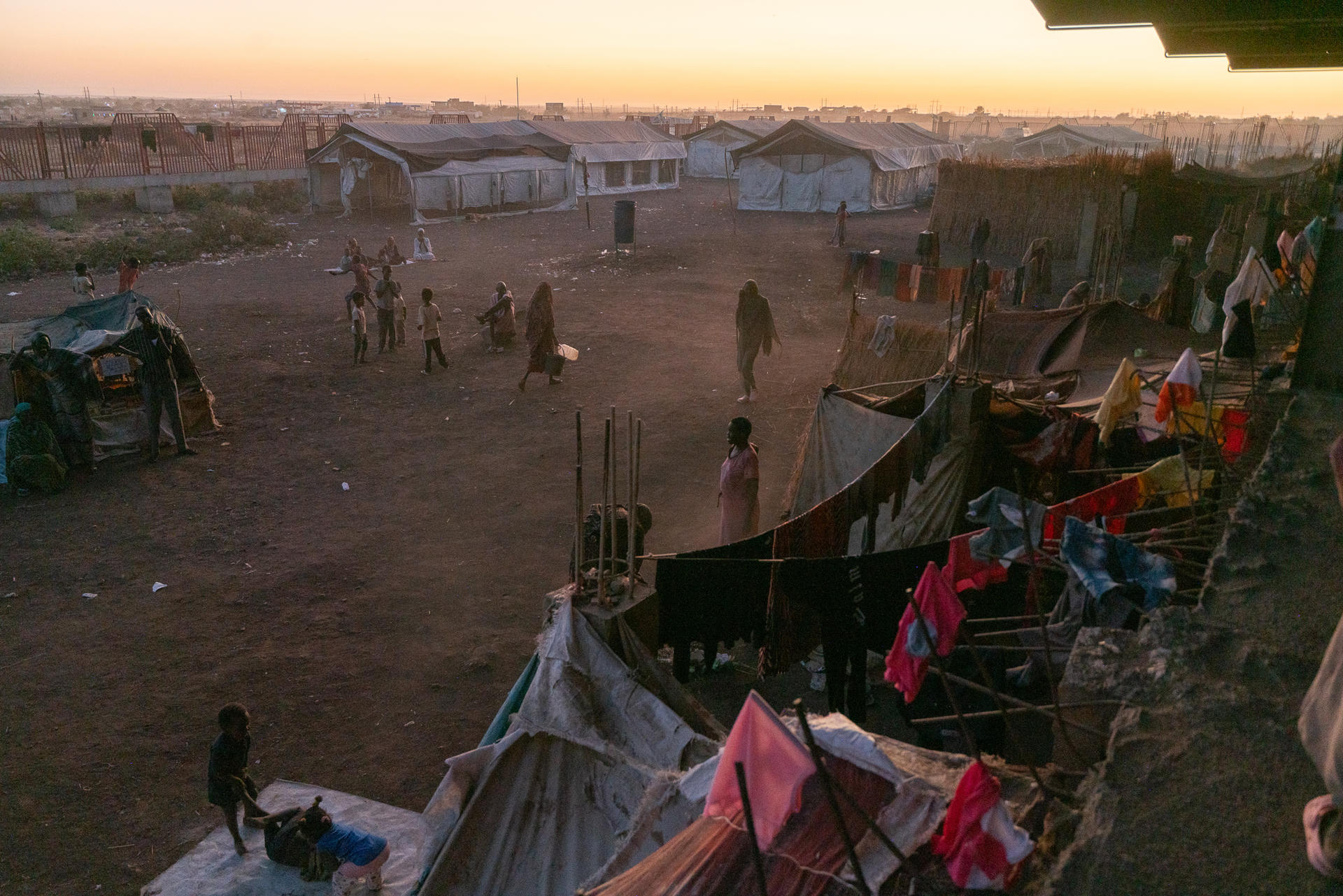 Dusty settlement at sunset with makeshift shelters and children playing.