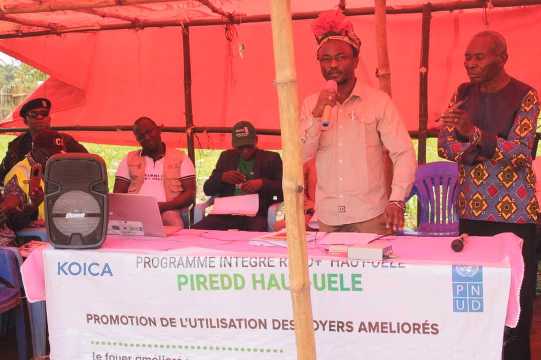 A group of people gathered under a tent, with one man speaking at a table displaying a banner.